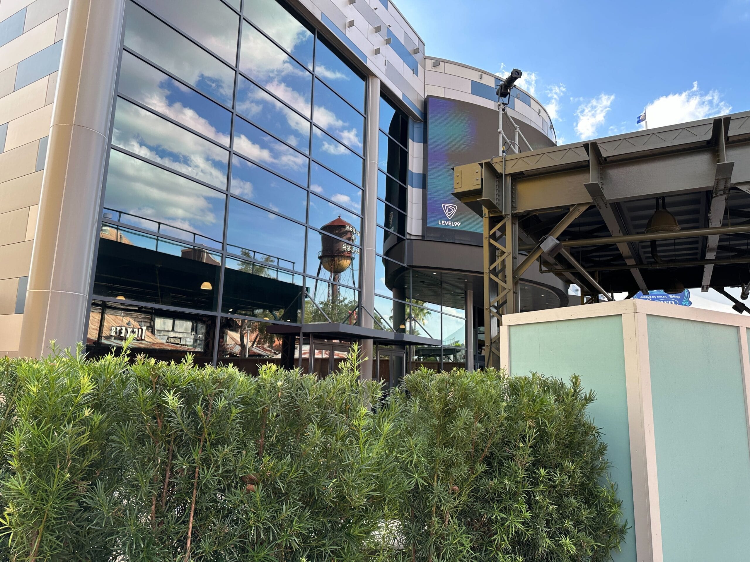 Modern glass building reflected with a water tower, green shrubs, and construction barriers—no castle like Disney park icons visible.