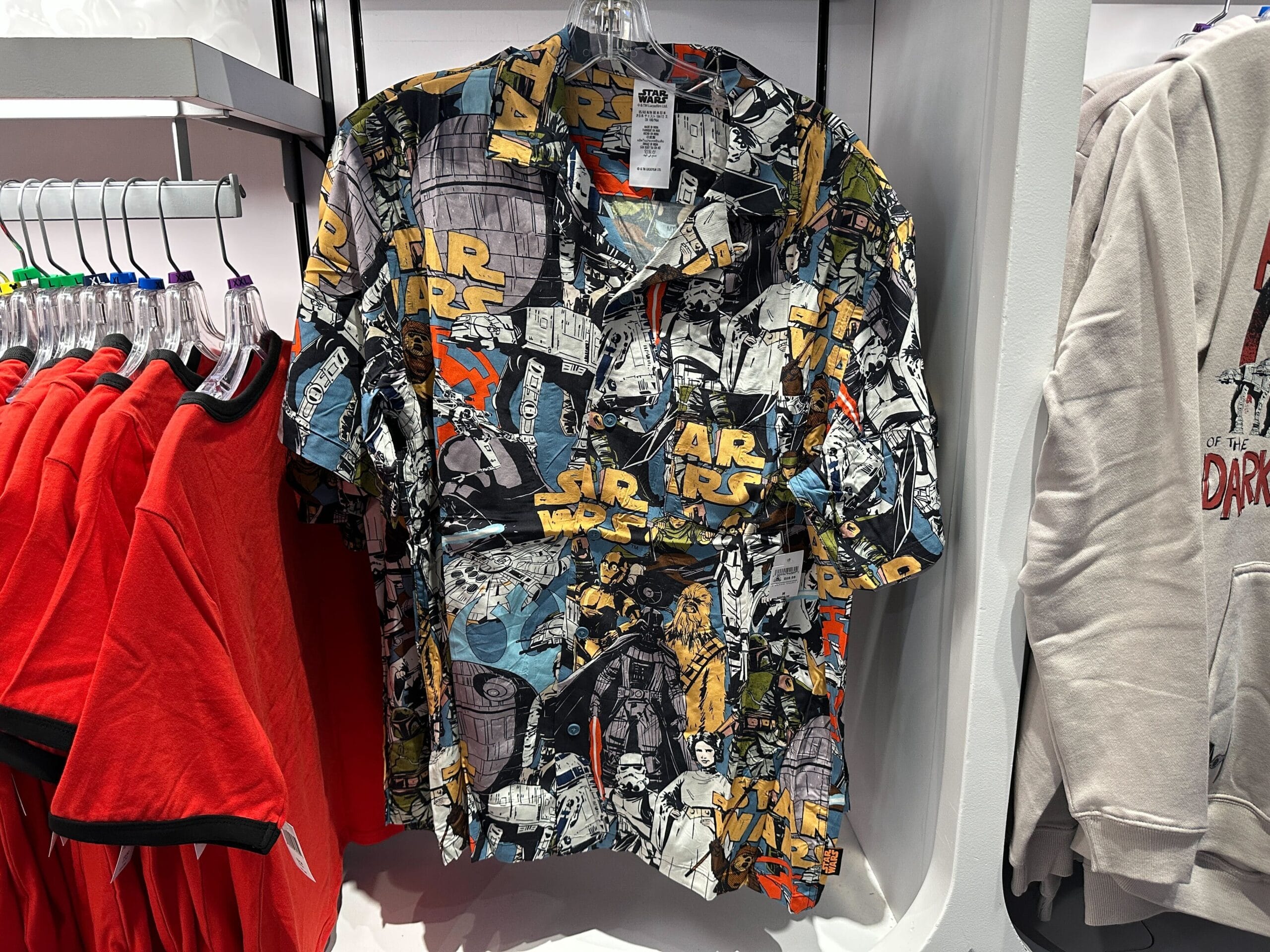 A vibrant Star Wars comic-style button-up shirt hangs on a rack at Disney World, surrounded by magical park merchandise.