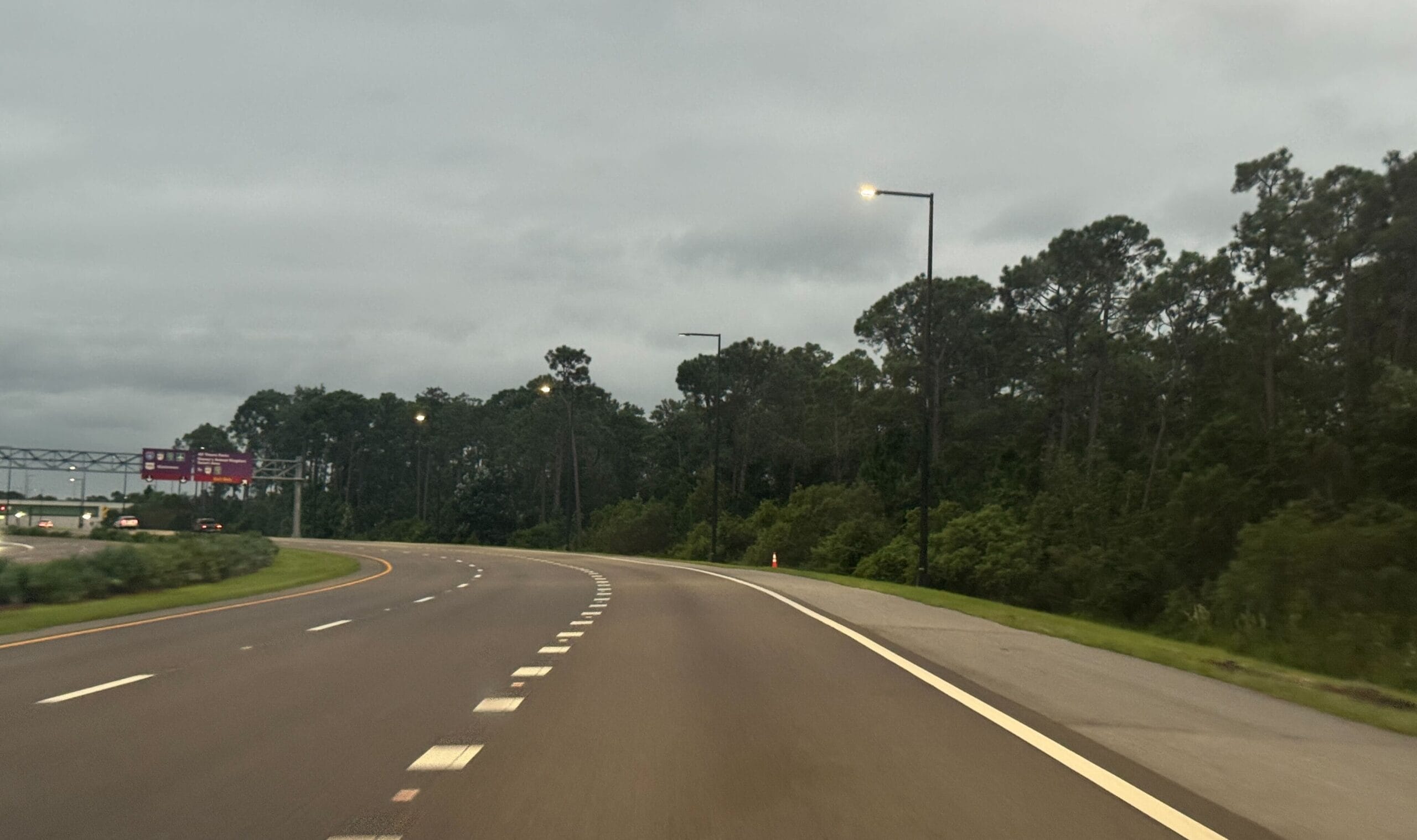 Curving highway with glowing streetlights, tree-lined, near Walt Disney World—no castle view like Cinderella Castle here; cloudy sky.