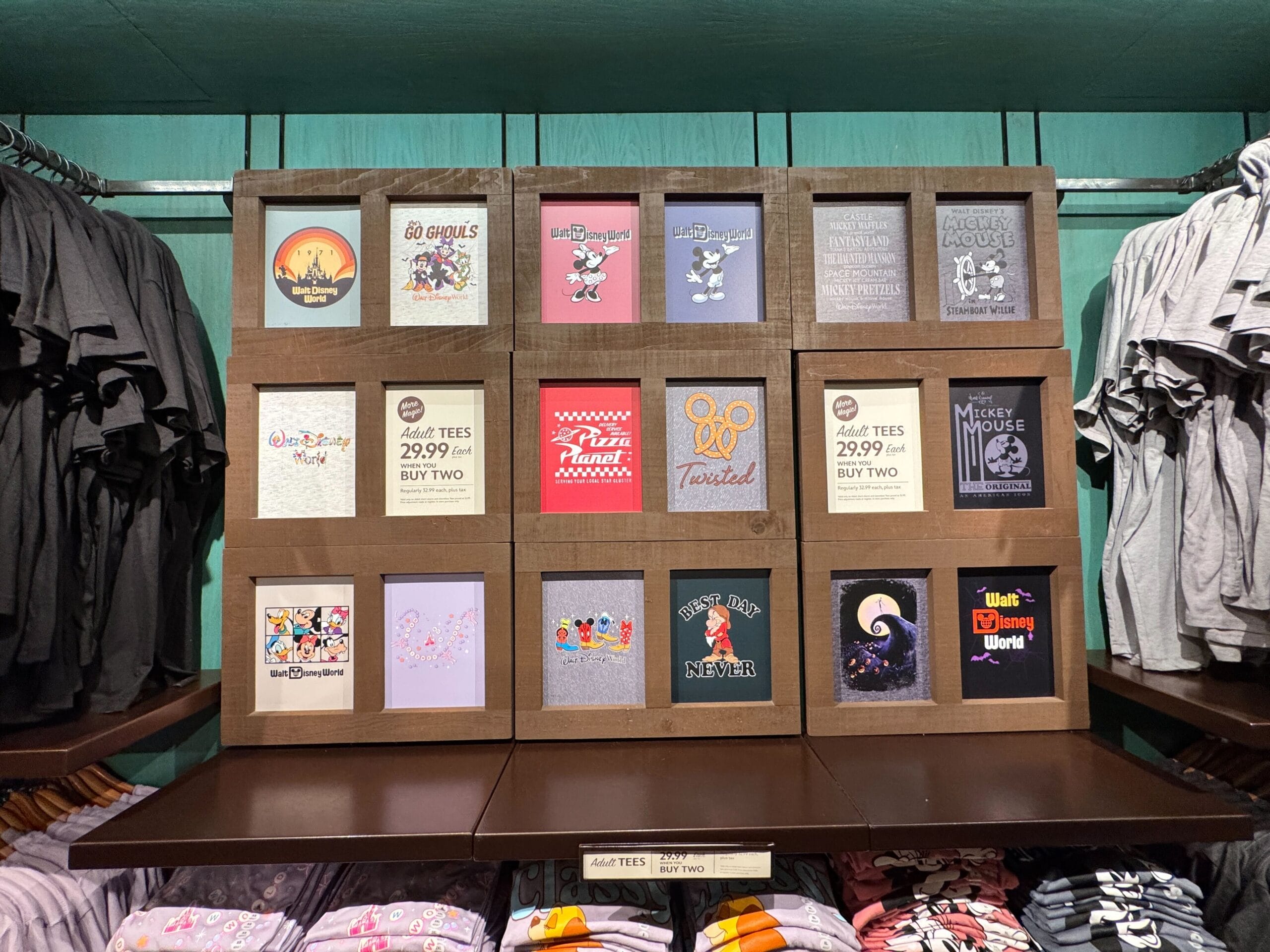 Display of folded graphic t-shirts with various Disney designs and prices, arranged in a wooden shelf at a store.