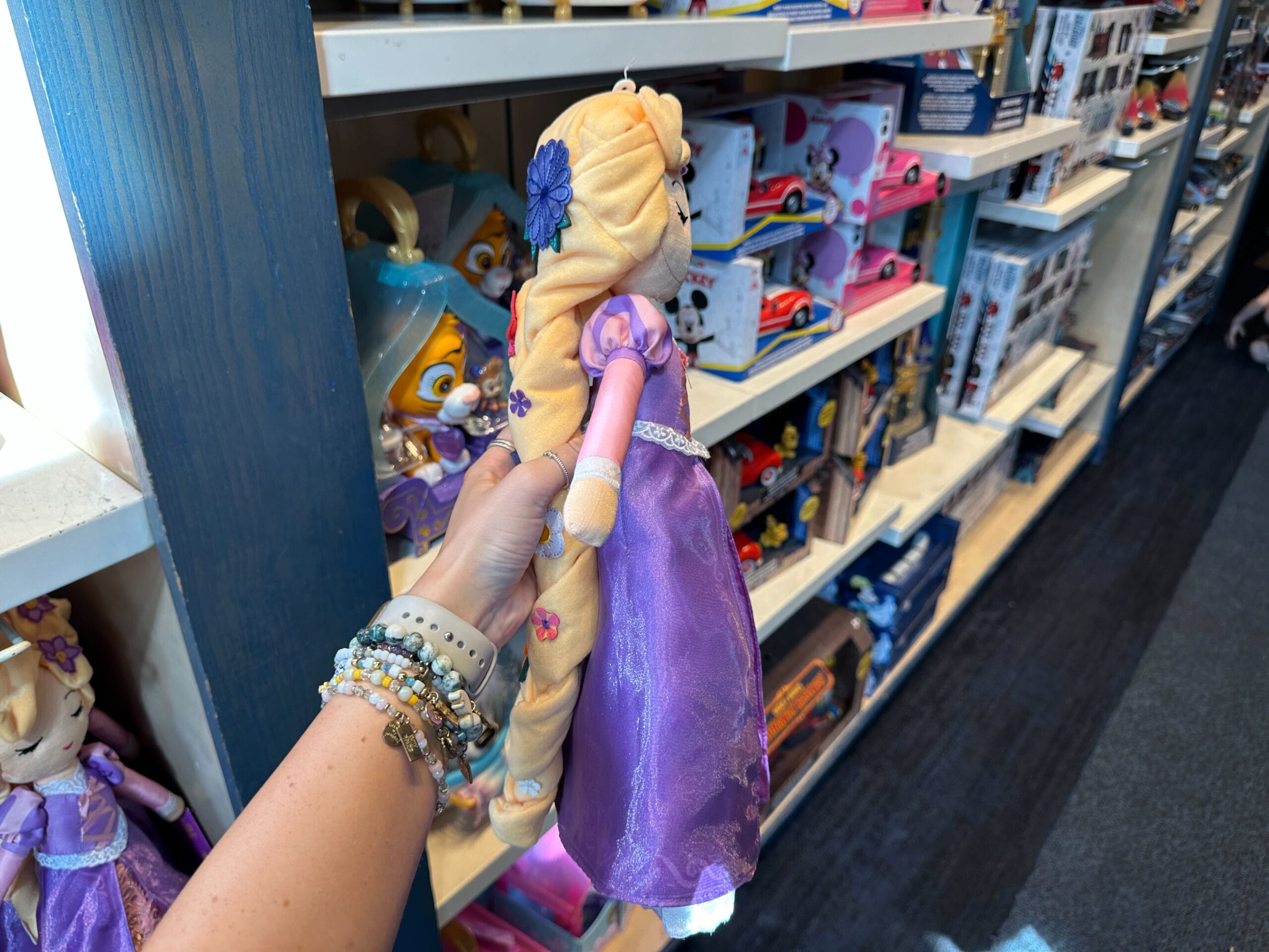 A person holds a Rapunzel doll with her signature long braid in a toy store aisle, similar to shops found on Main Street in Disney parks.