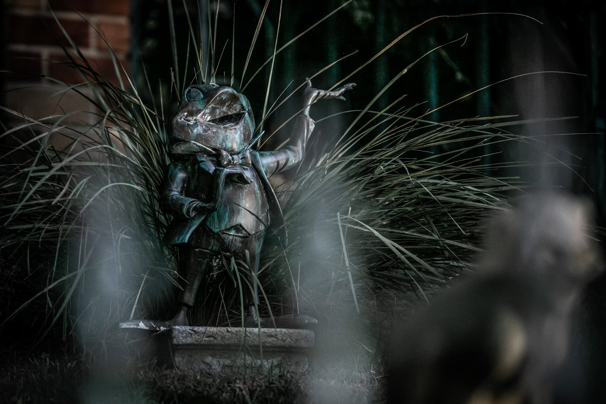A bronze frog in a suit stands tall, evoking Haunted Mansion vibes—like a whimsical sight from Disneyland’s gardens.
