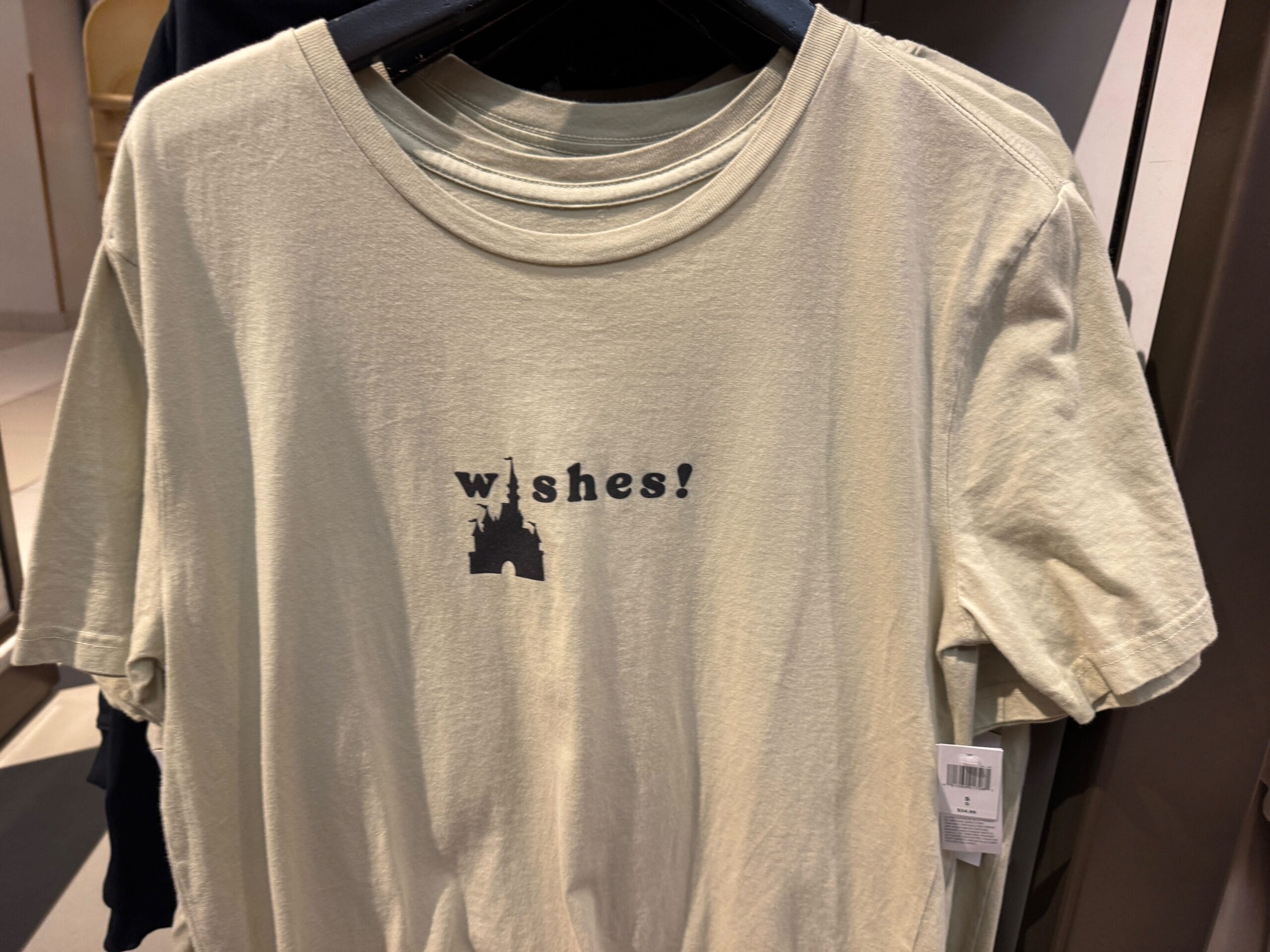 Light beige T-shirt with "wishes!" and a small castle silhouette below, resembling Cinderella Castle at Walt Disney World.