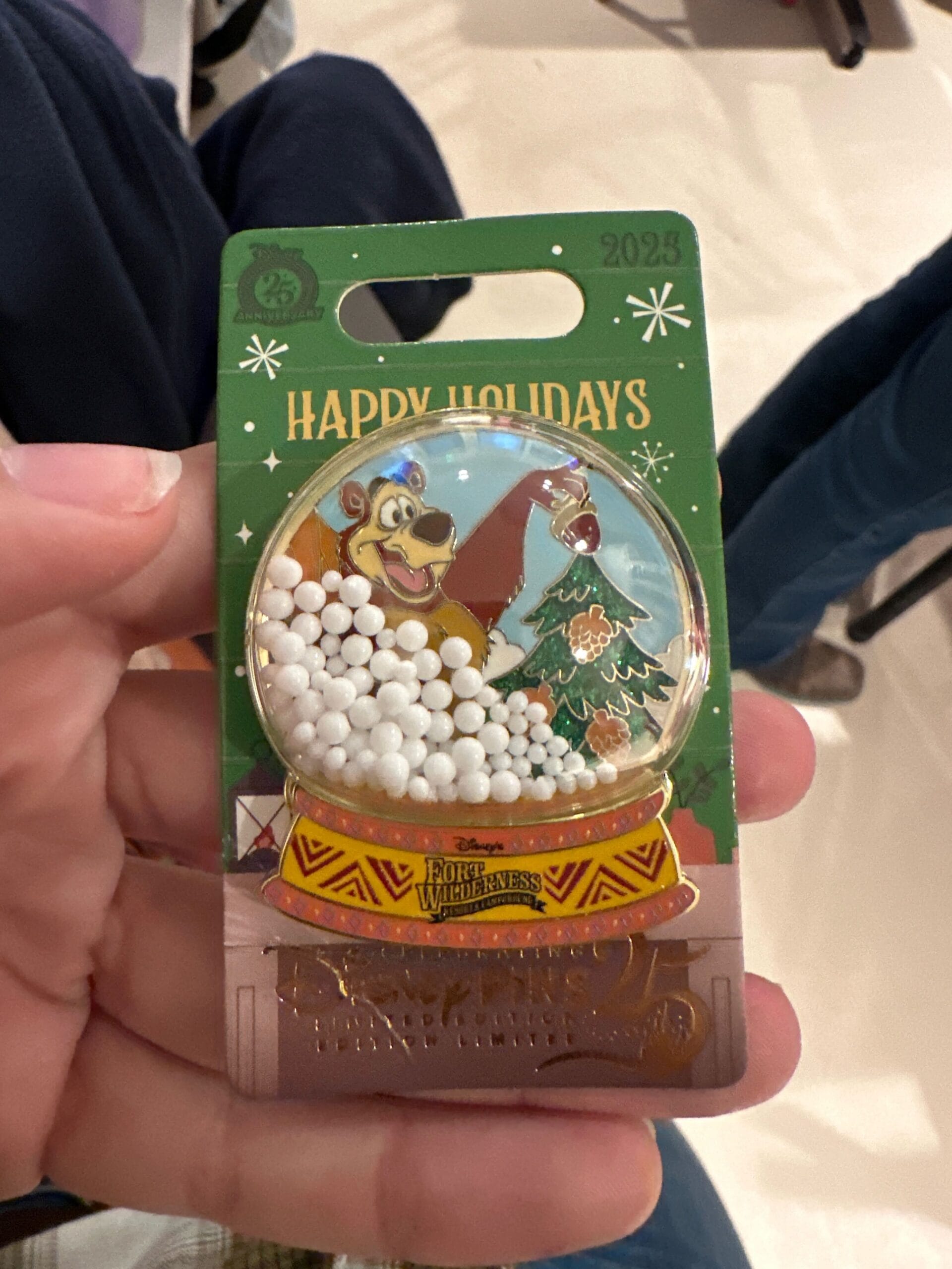 A hand displays a Walt Disney World Fort Wilderness Resort holiday pin featuring a bear, tree, and snow globe—no castle depicted.