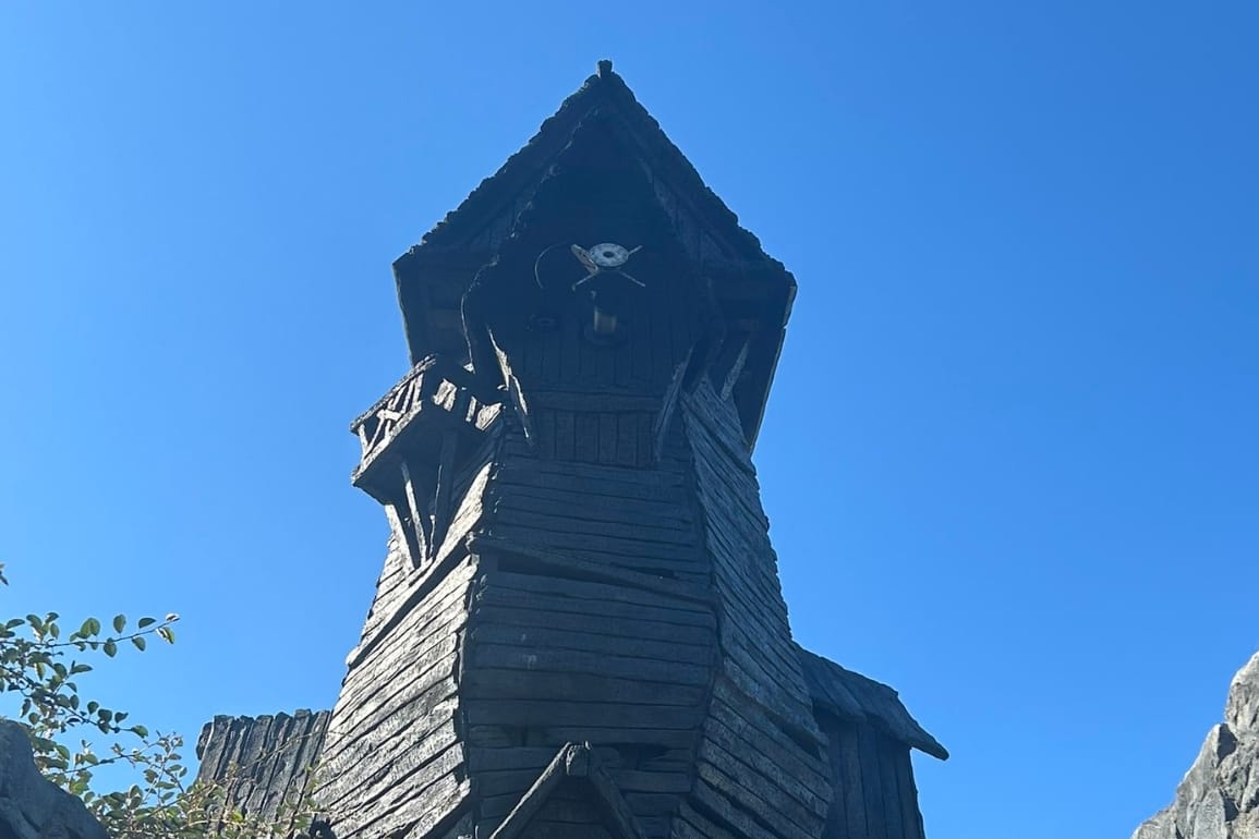 A tall, dark wooden tower with a pointed roof—reminiscent of Disney castle turrets—stands against an Epic Universe sky.