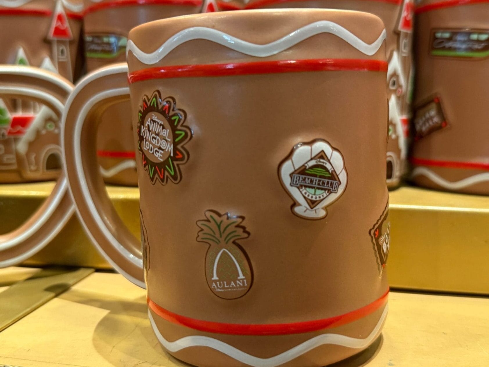 A brown ceramic mug with souvenir pins, featuring resort gingerbread designs, displayed on a Disney Parks merchandise shelf.