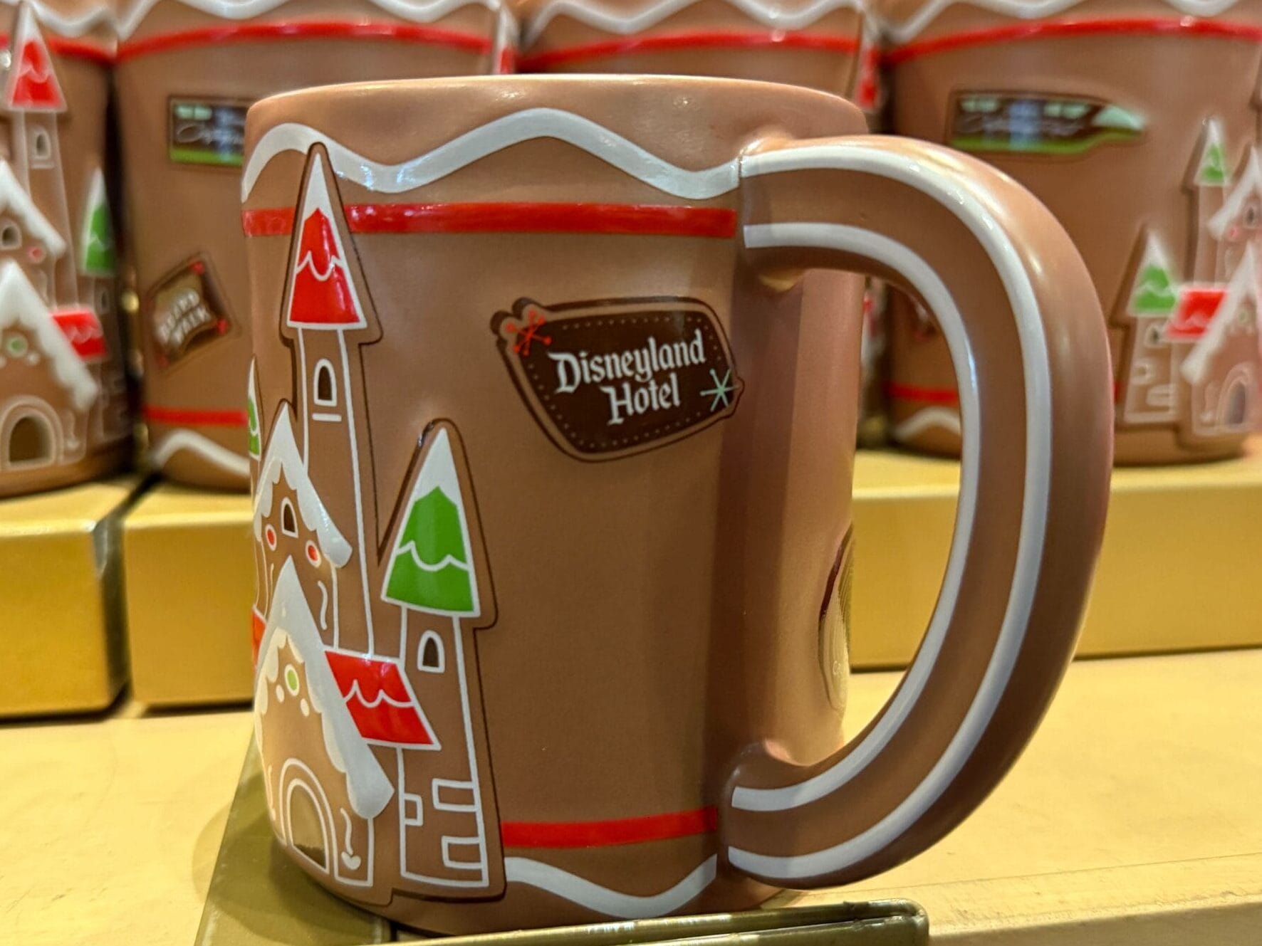 Brown Disneyland Resort hotel mug featuring a castle resembling Sleeping Beauty Castle, with trees; more mugs on shelf behind.