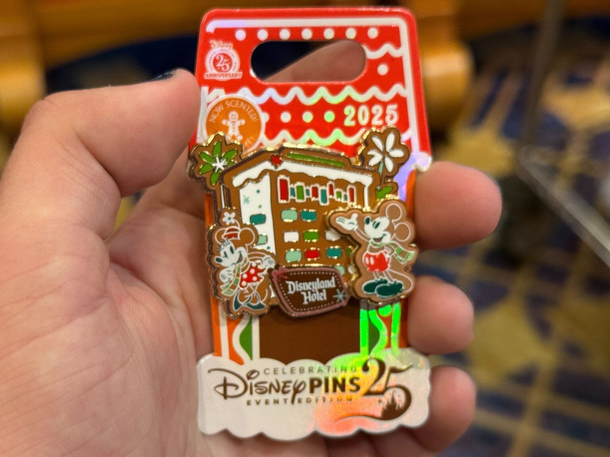 A hand displays a Disneyland Hotel 2025 pin featuring Mickey and Minnie in festive resort attire, no castle like Disneyland Paris’s.