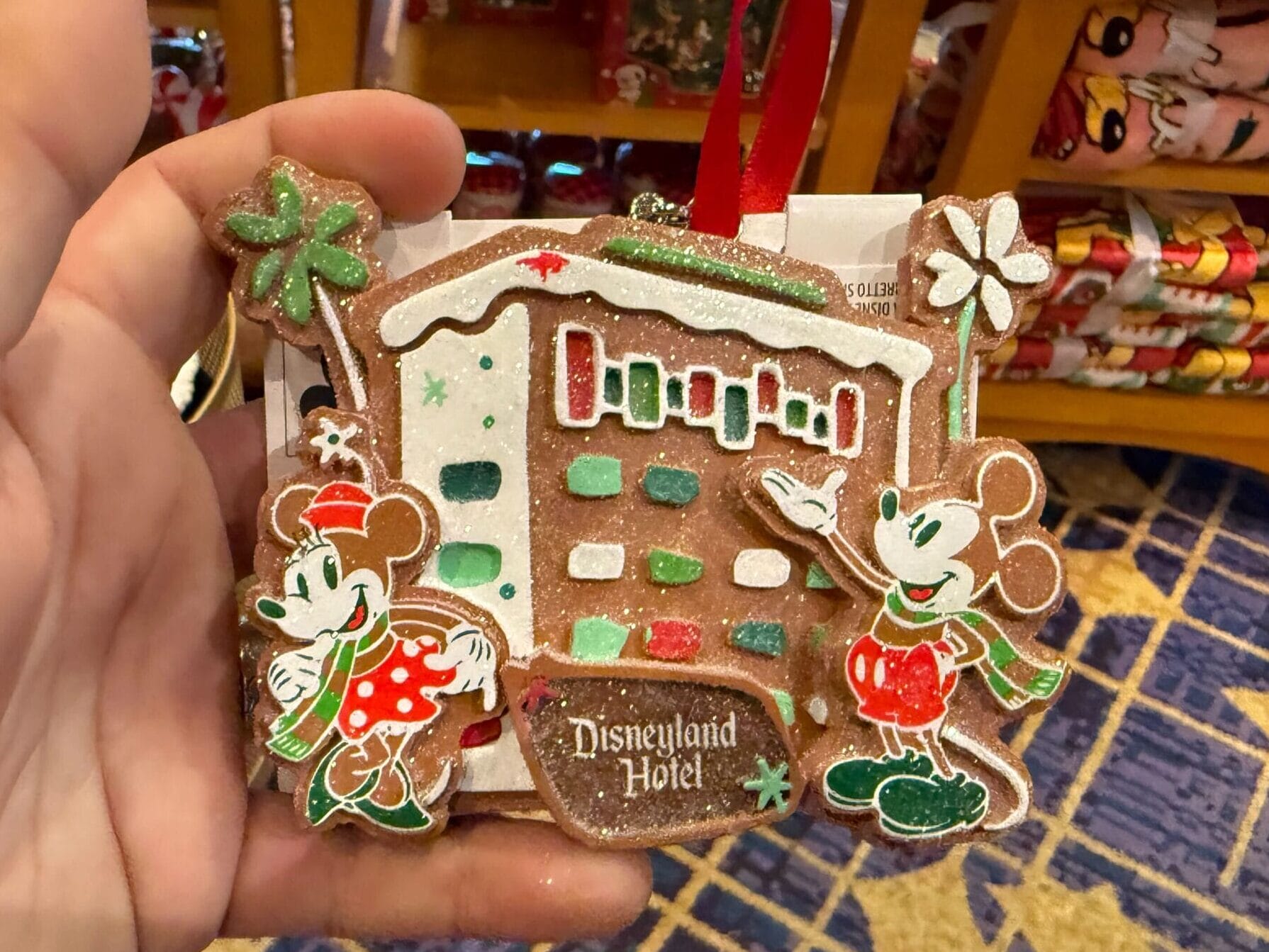 Hand holding a Disneyland Hotel gingerbread ornament with Minnie and Mickey in festive outfits, evoking park holiday decor vibes.