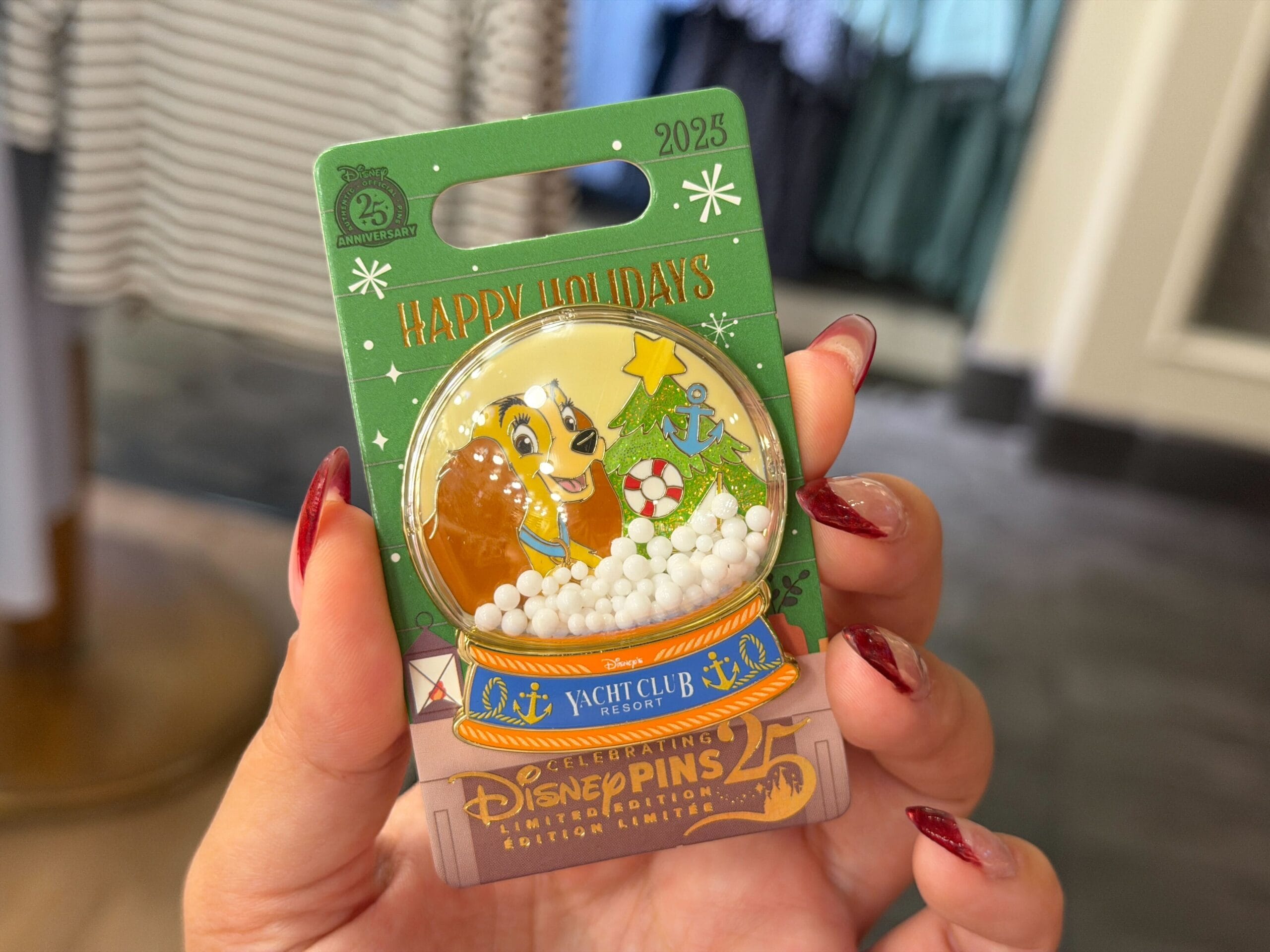 A hand holds a Walt Disney World Yacht Club 2025 holiday pin with Lady in a festive snow globe, exclusive to this Florida resort.