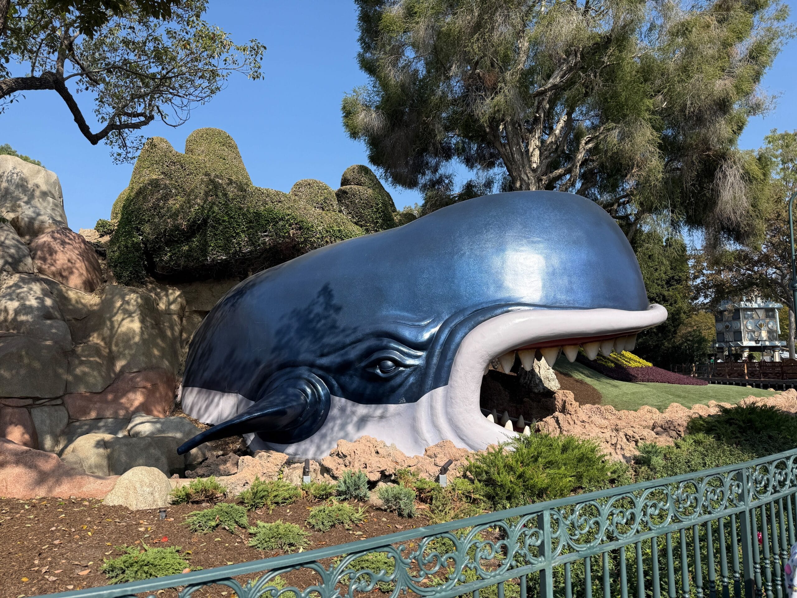 A large blue whale statue with its mouth open, surrounded by lush landscaping, similar to Disneyland's Storybook Land Canal Boats.