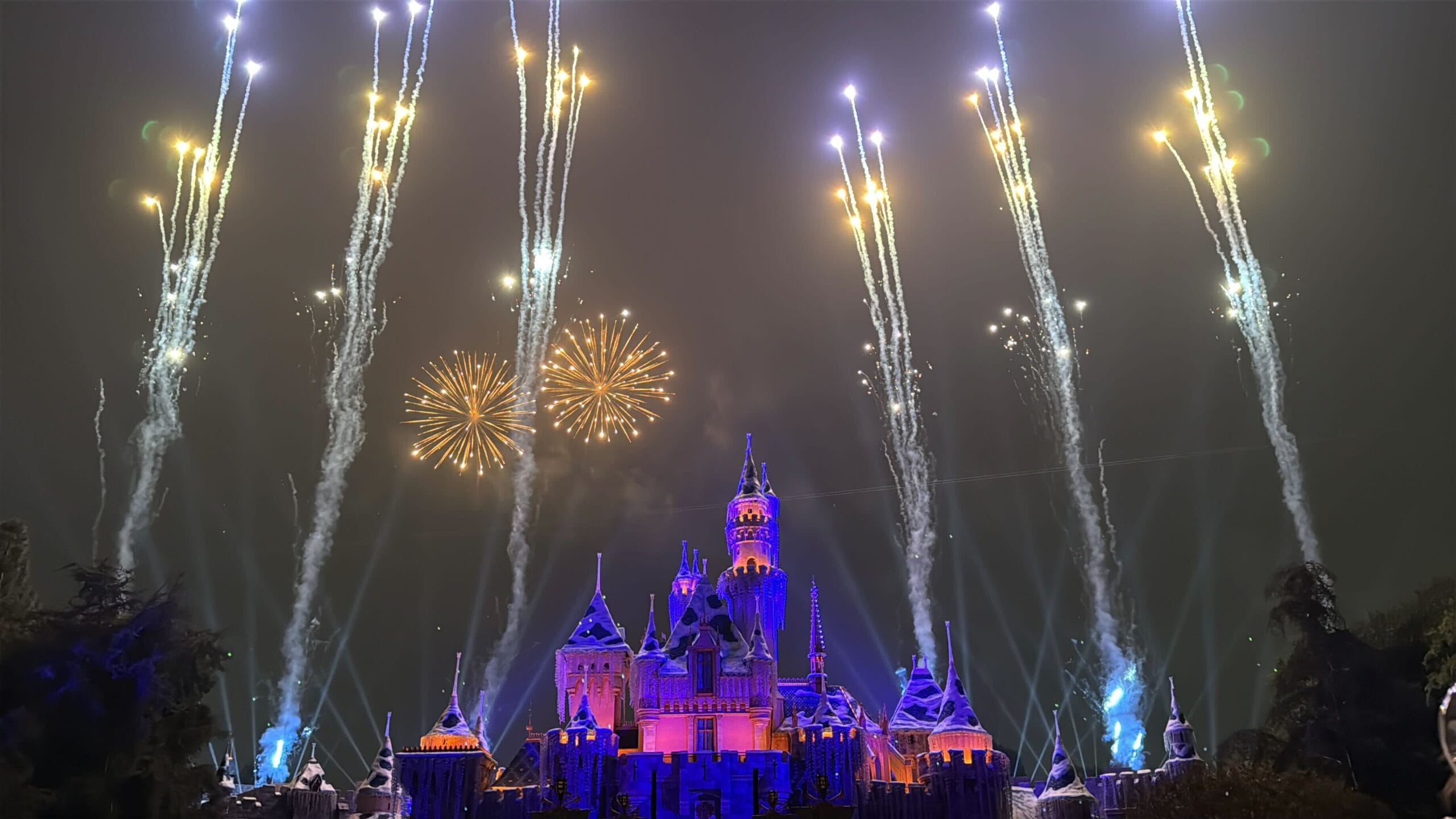 Fireworks and spotlights dazzle above Disneyland’s castle, reminiscent of the Anaheim Sleeping Beauty Castle, lighting the night sky.