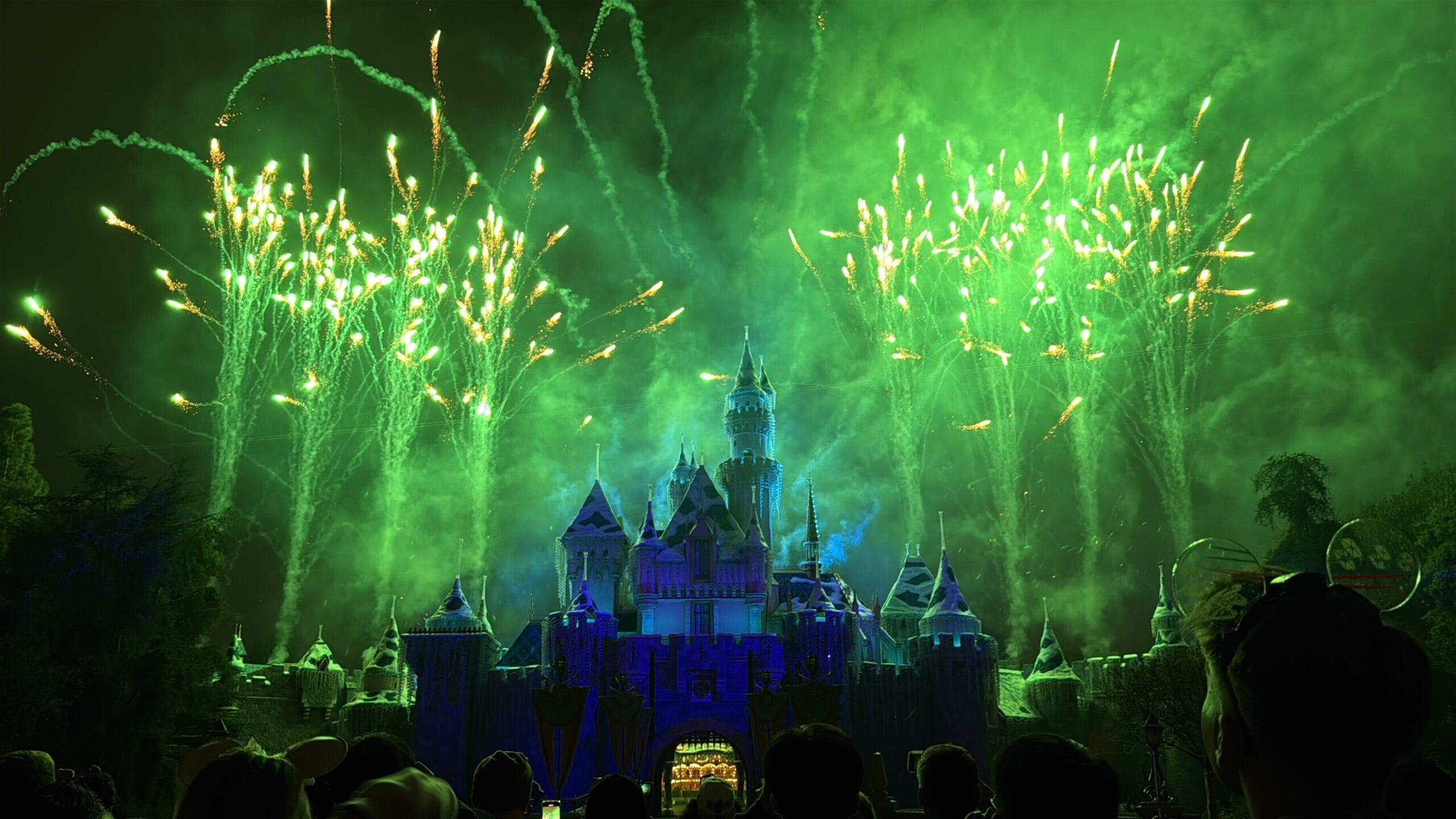 Green fireworks burst above Disneyland’s iconic castle, its design unique from Disney World’s Cinderella Castle, dazzling the Wondrous Journeys crowd.