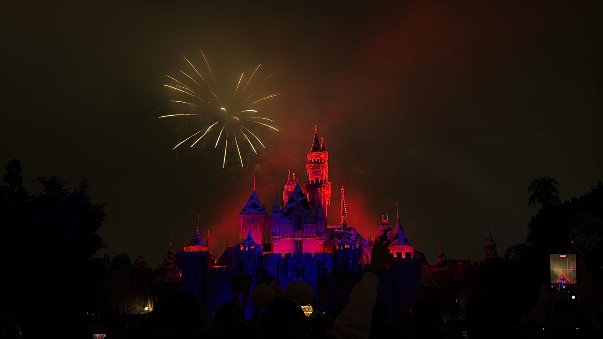 Sleeping Beauty Castle at Disneyland, aglow in red and blue lights during Wondrous Journeys fireworks—smaller than Cinderella Castle.