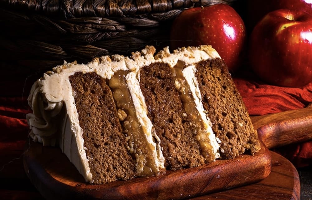 A spiced layer cake slice from Gideon's Bakehouse, topped with apples and frosting, sits on a board in Disney Springs.