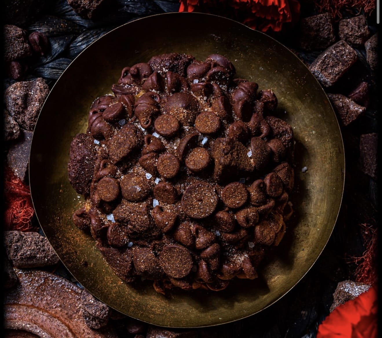 A rich Gideon's Bakehouse chocolate chip cookie on a brass plate, surrounded by chocolate pieces, just like at Disney Springs.