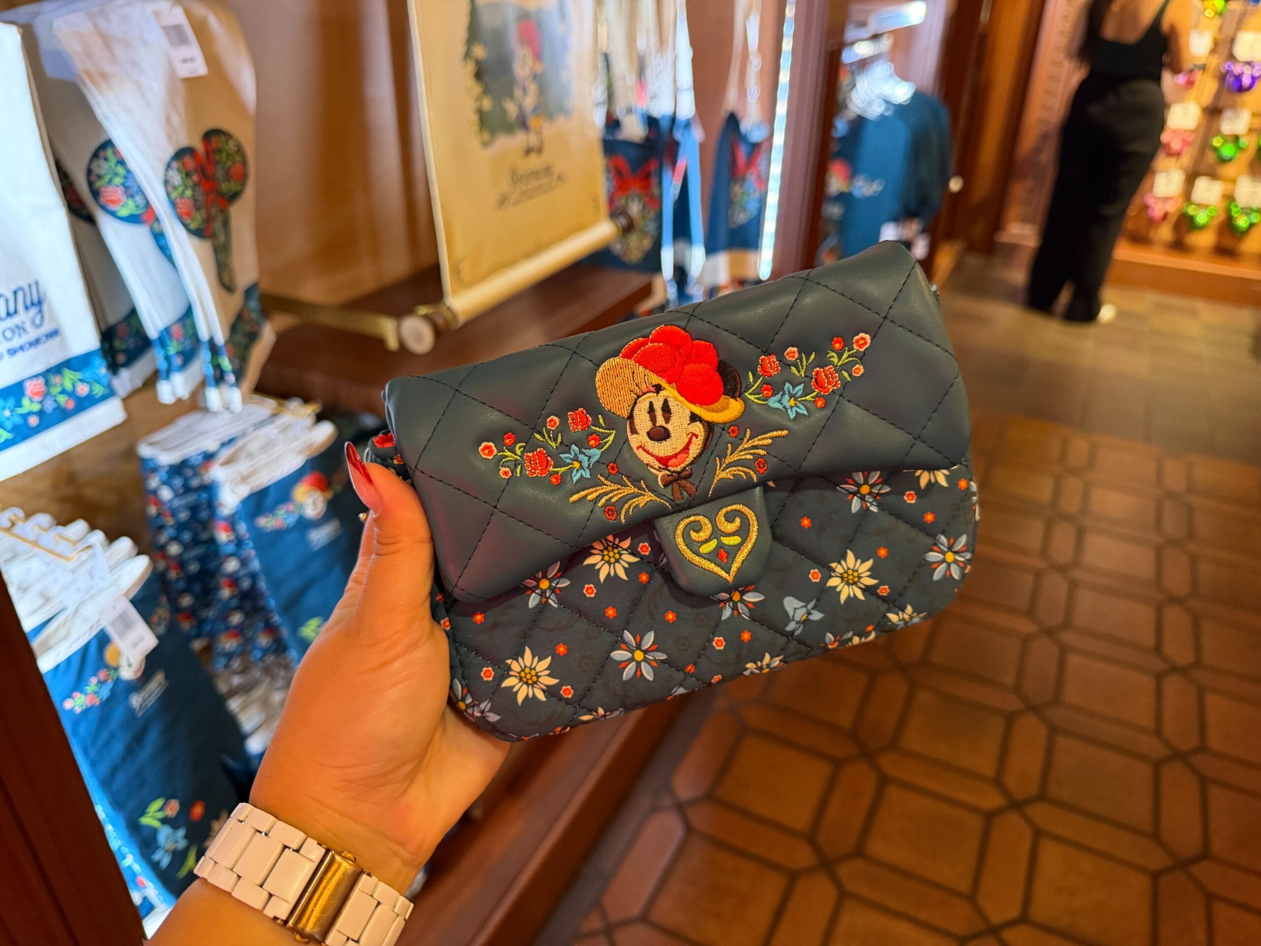 Hand holding a quilted purse with Minnie Mouse and floral embroidery, from Germany Epcot merch at a Disney park store.