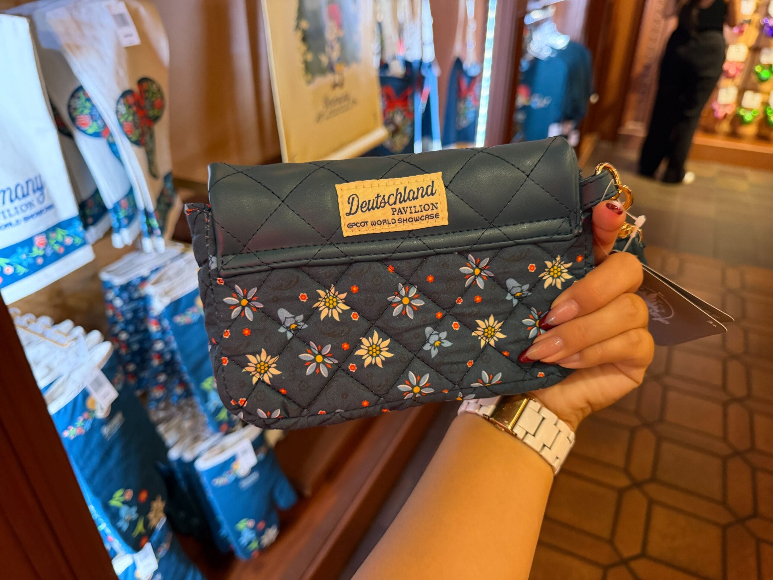 A hand holds a floral-embroidered Deutschland Pavilion purse, classic EPCOT merch found in Germany’s gift shop, no castle in view.