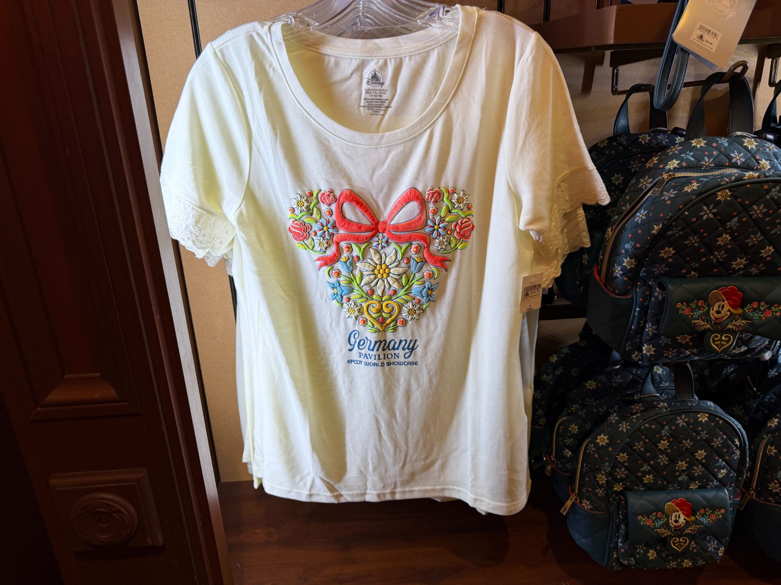 White T-shirt with floral heart and red bow, Germany Merch at Epcot, inspired by the Black Forest—no castle like at Disney parks.