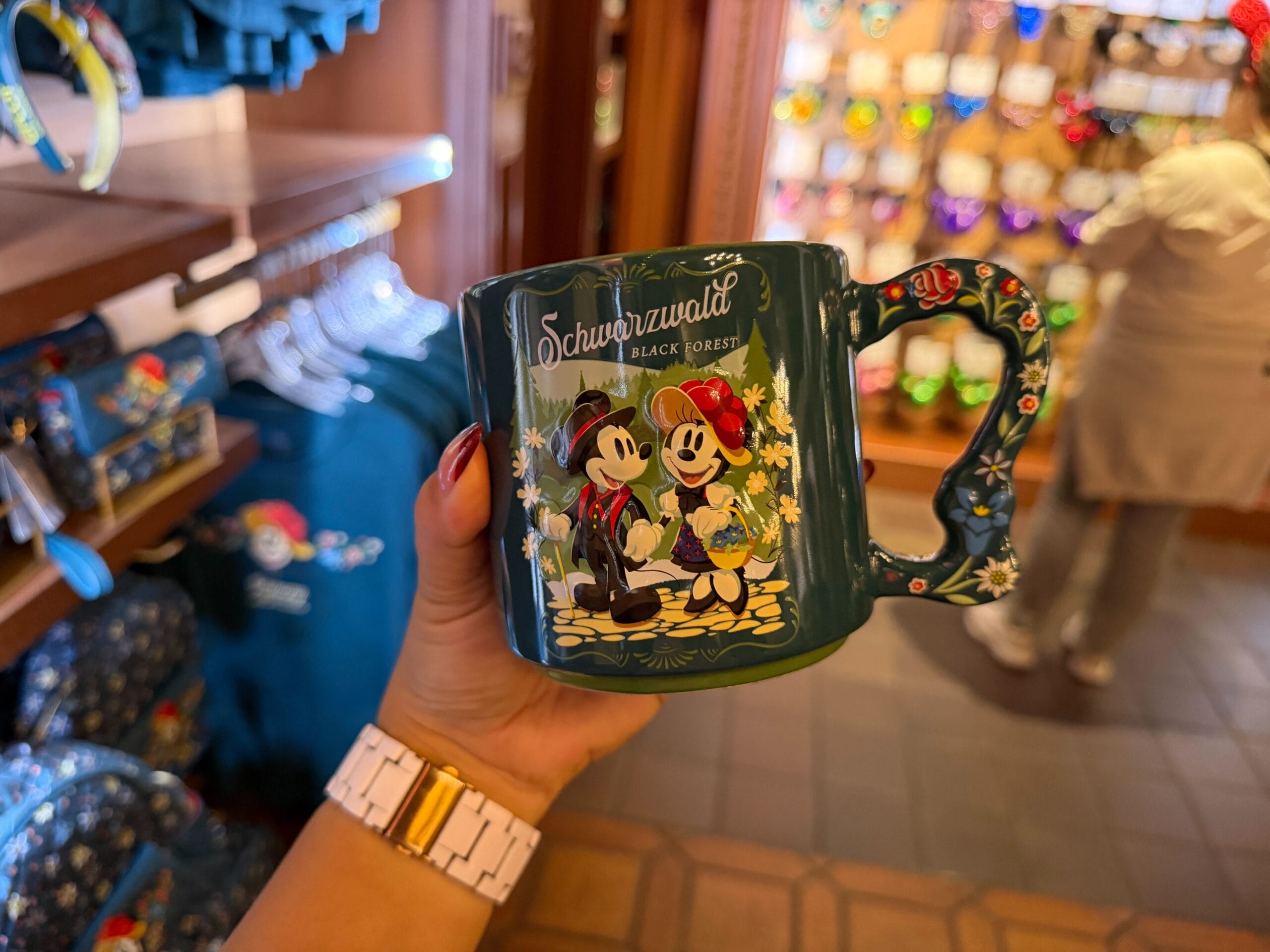 Hand holding Black Forest mug with Mickey & Minnie Mouse at Epcot’s Germany shop, reminiscent of Disney park exclusive merch.
