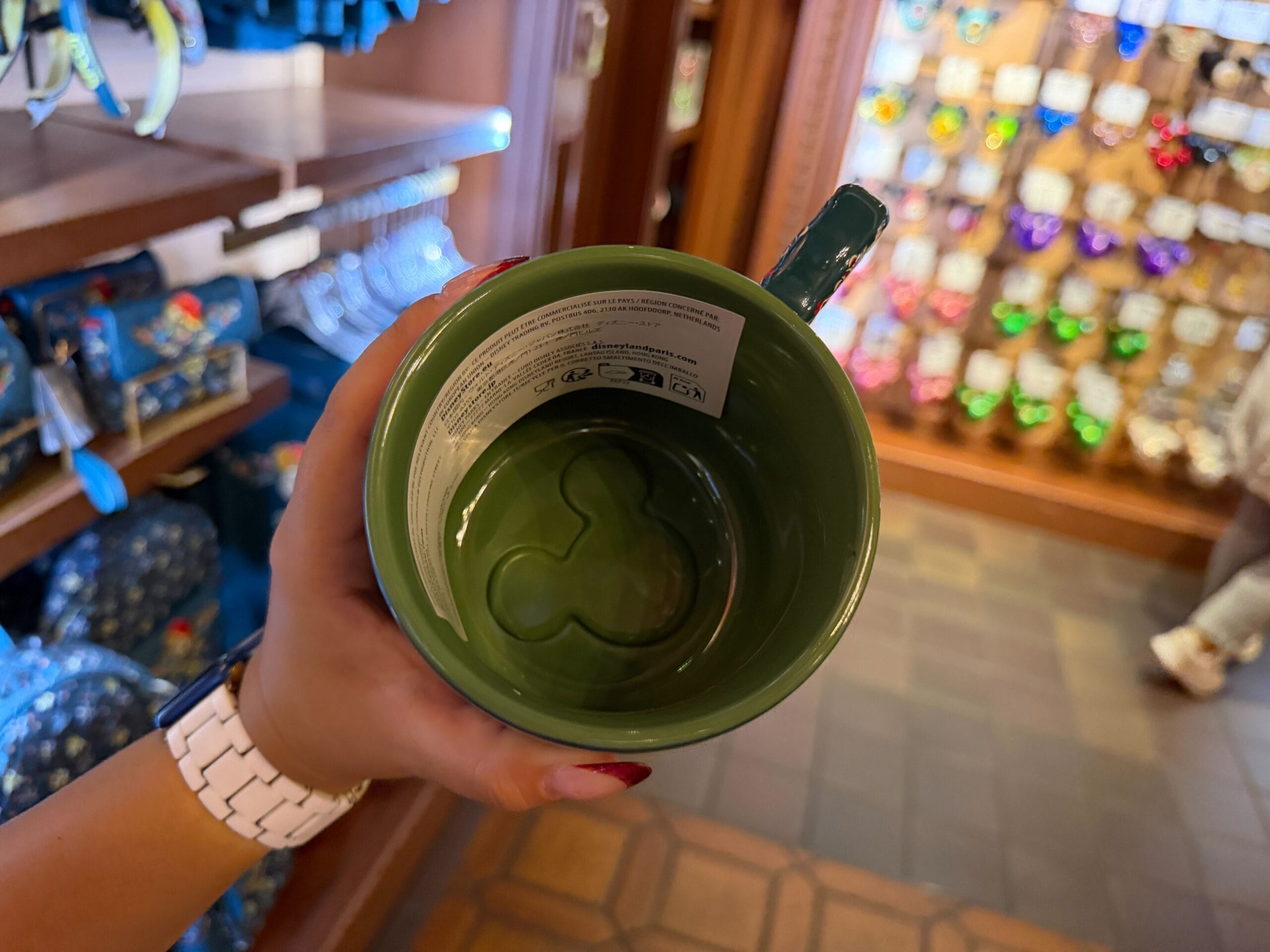 A hand holds a green mug featuring a Mickey Mouse shape inside, spotted in the Germany Pavilion shop at Epcot with Disney merch.