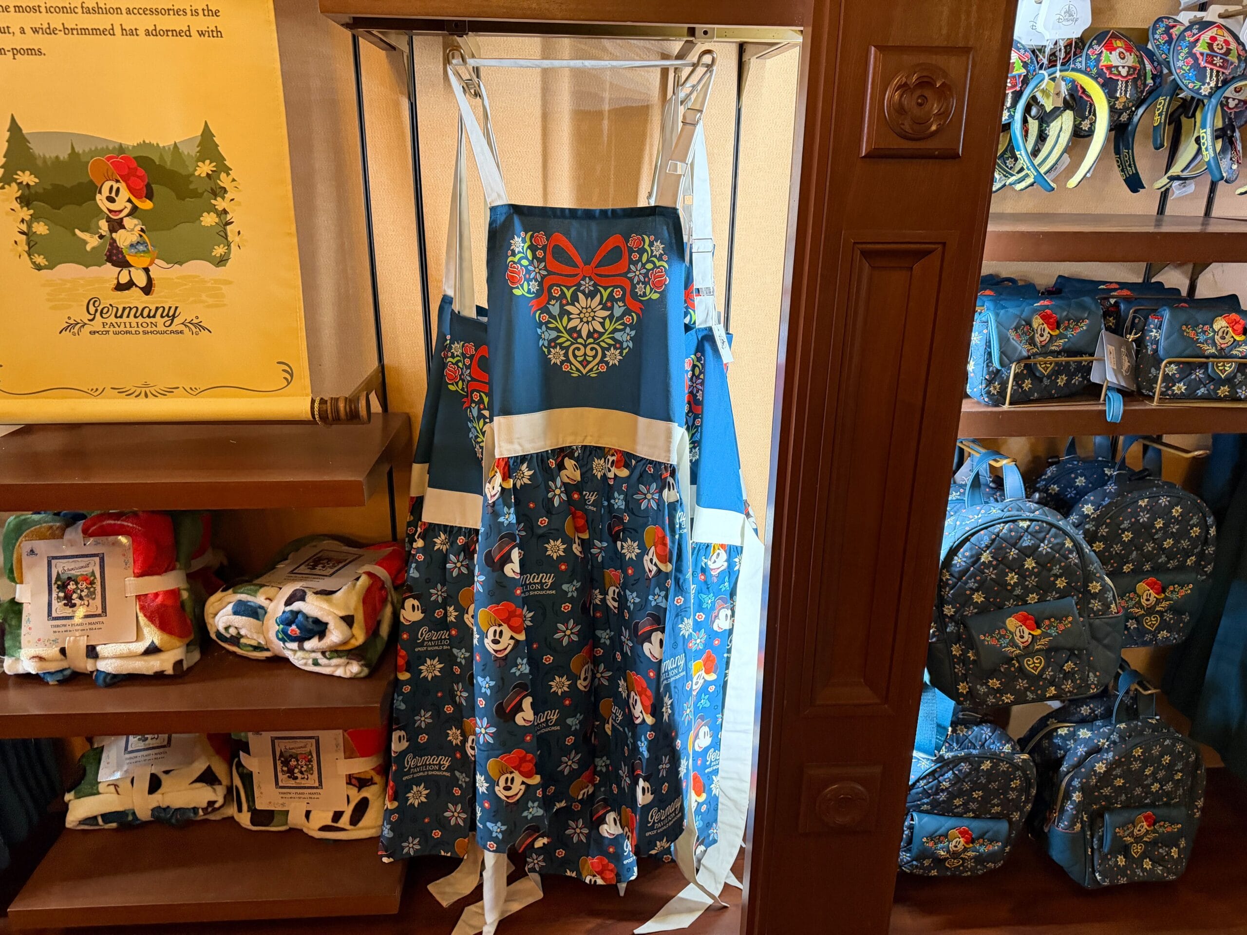 Blue apron with floral patterns and red bow, inspired by Black Forest Disney Parks merch, displayed with matching bags in-store.