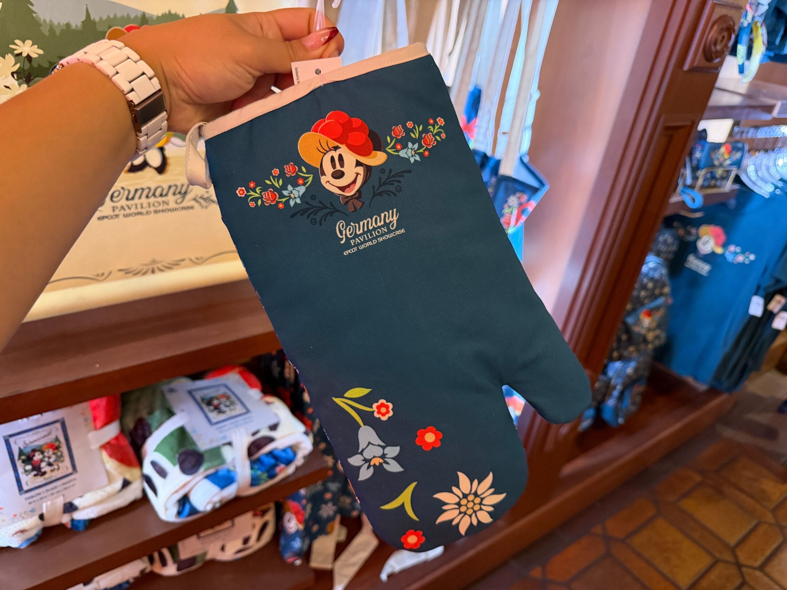 A hand displays a blue Minnie Mouse floral oven mitt from the Germany Pavilion at EPCOT, not far from Cinderella Castle’s park.