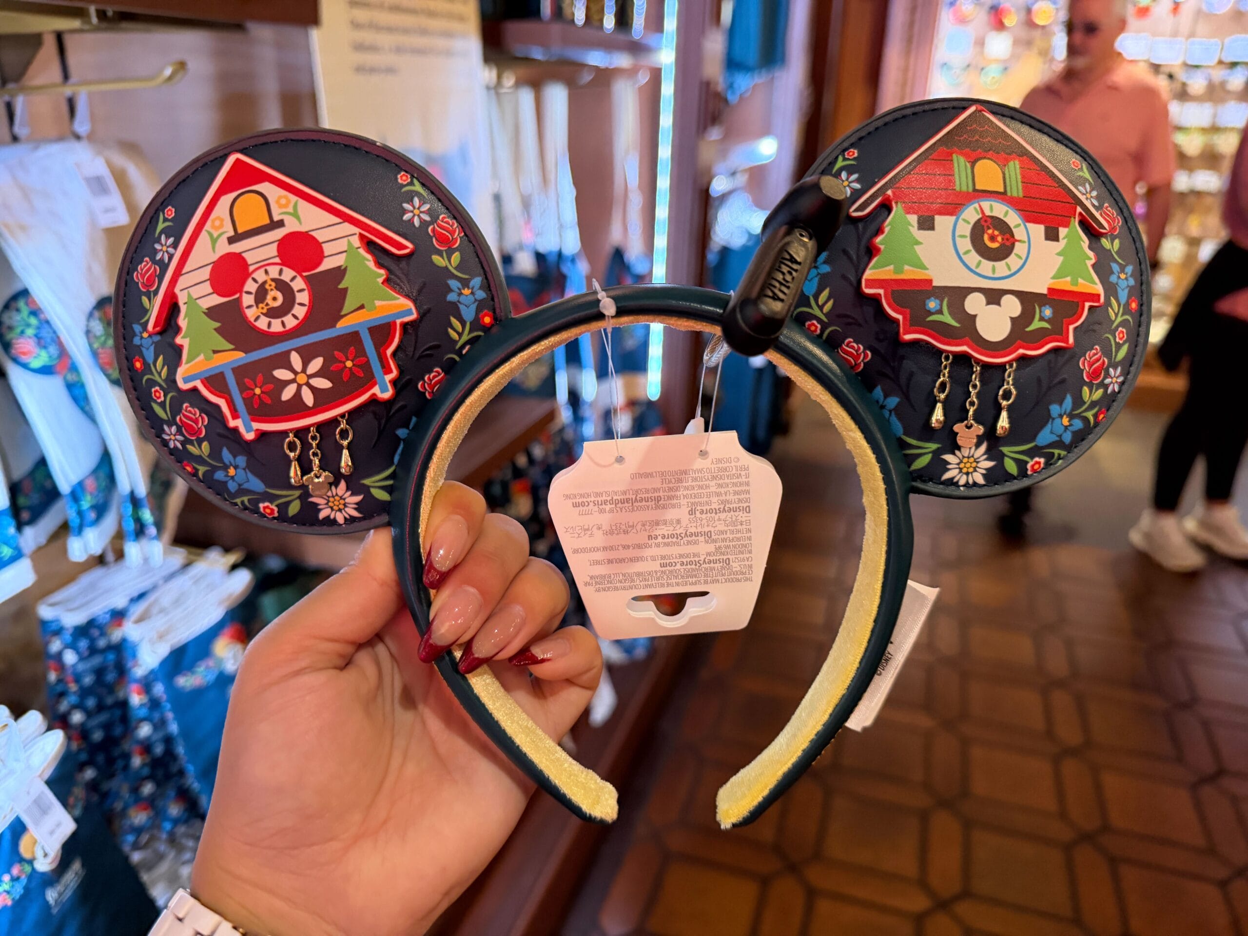 Germany Black Forest Mickey ear headband with cuckoo clocks and trees held in Disney merch shop—reminds of EPCOT’s Germany pavilion.