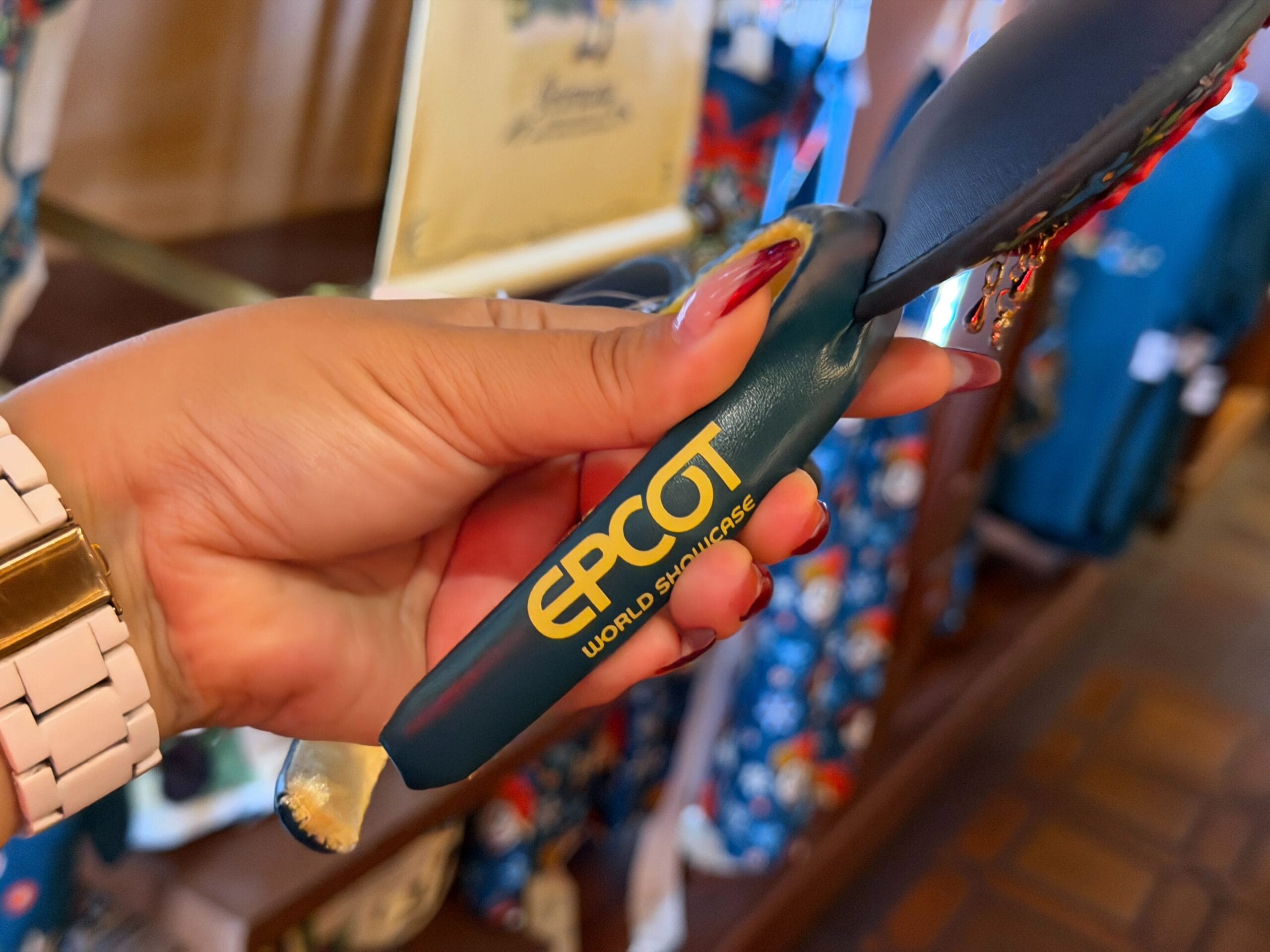 A hand holds a teal Germany-themed EPCOT spatula with "EPCOT WORLD SHOWCASE" in yellow, a fun Disney Parks kitchen souvenir.