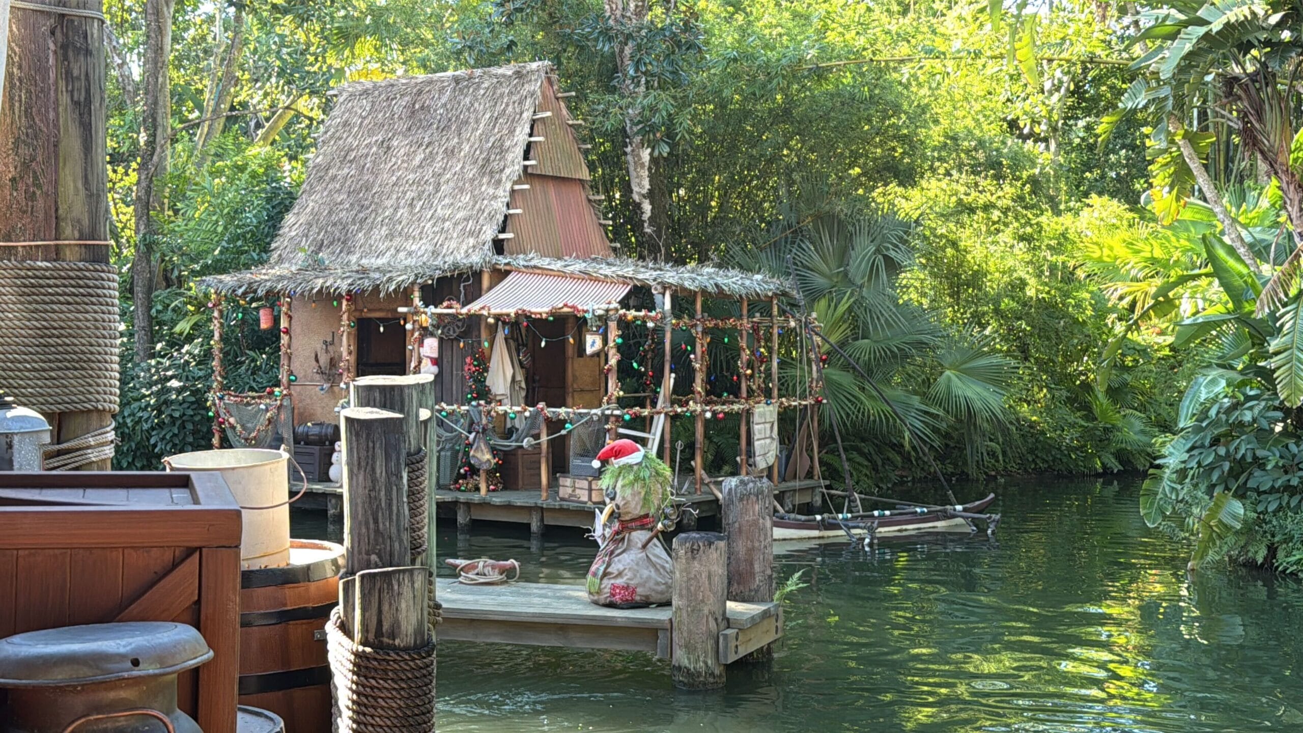 A festive Jingle Cruise hut sparkles with string lights by the water, surrounded by greenery at Magic Kingdom for Christmas 2025.