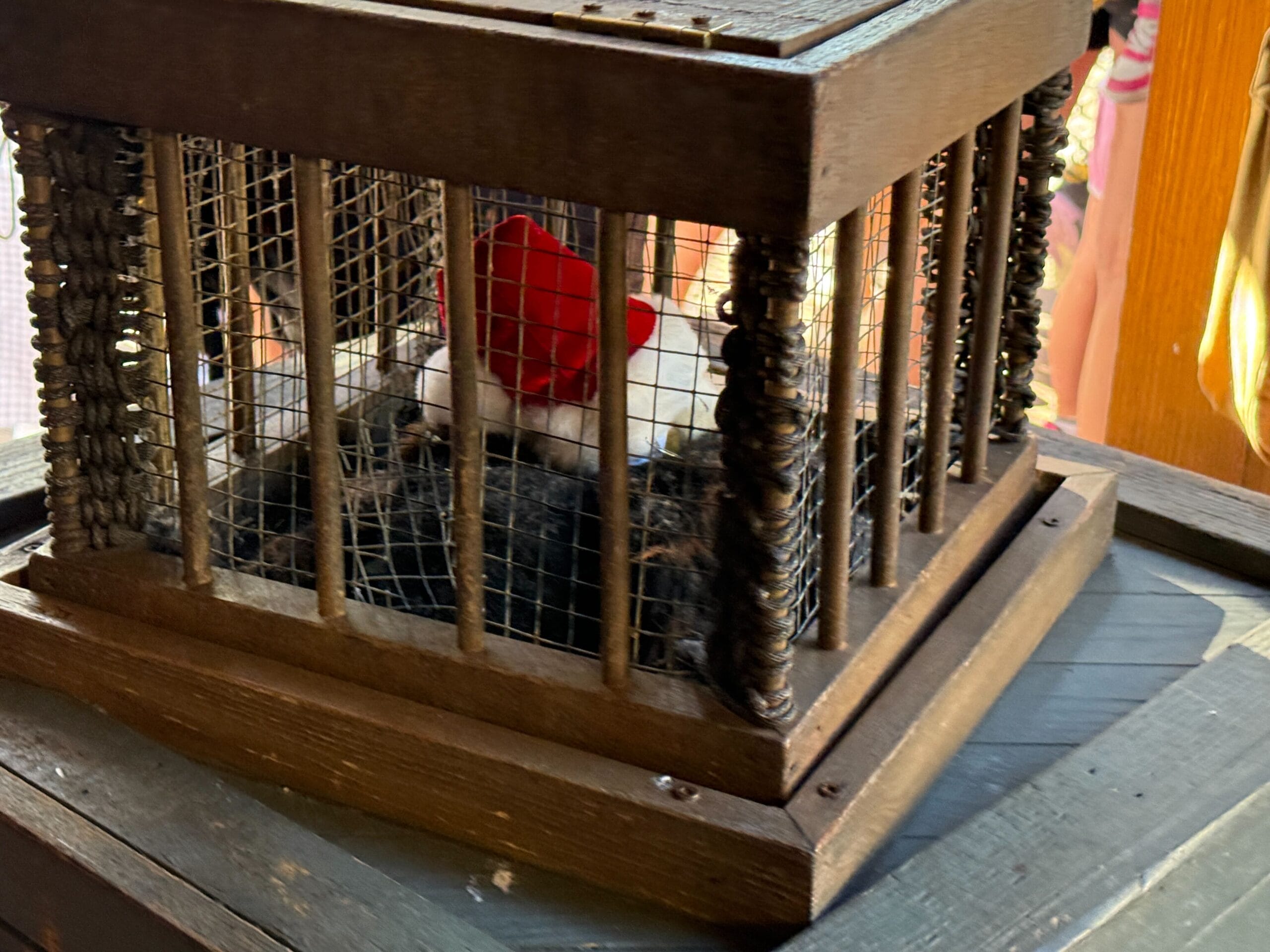 A plush white mouse in a red hat sits in a wooden display, evoking Magic Kingdom Christmas cheer