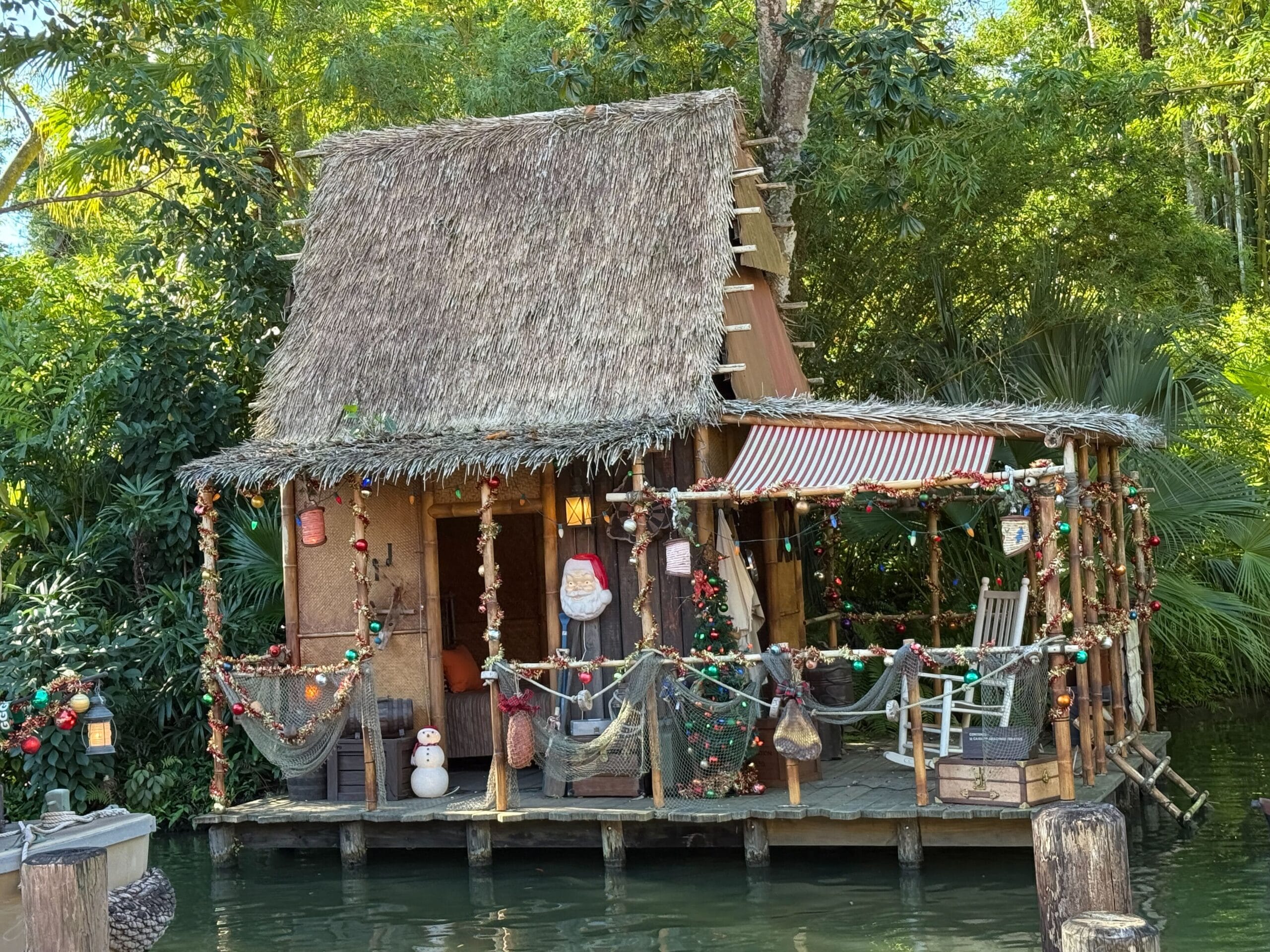 A thatched hut overlooking water at Magic Kingdom sparkles with Christmas lights and garlands