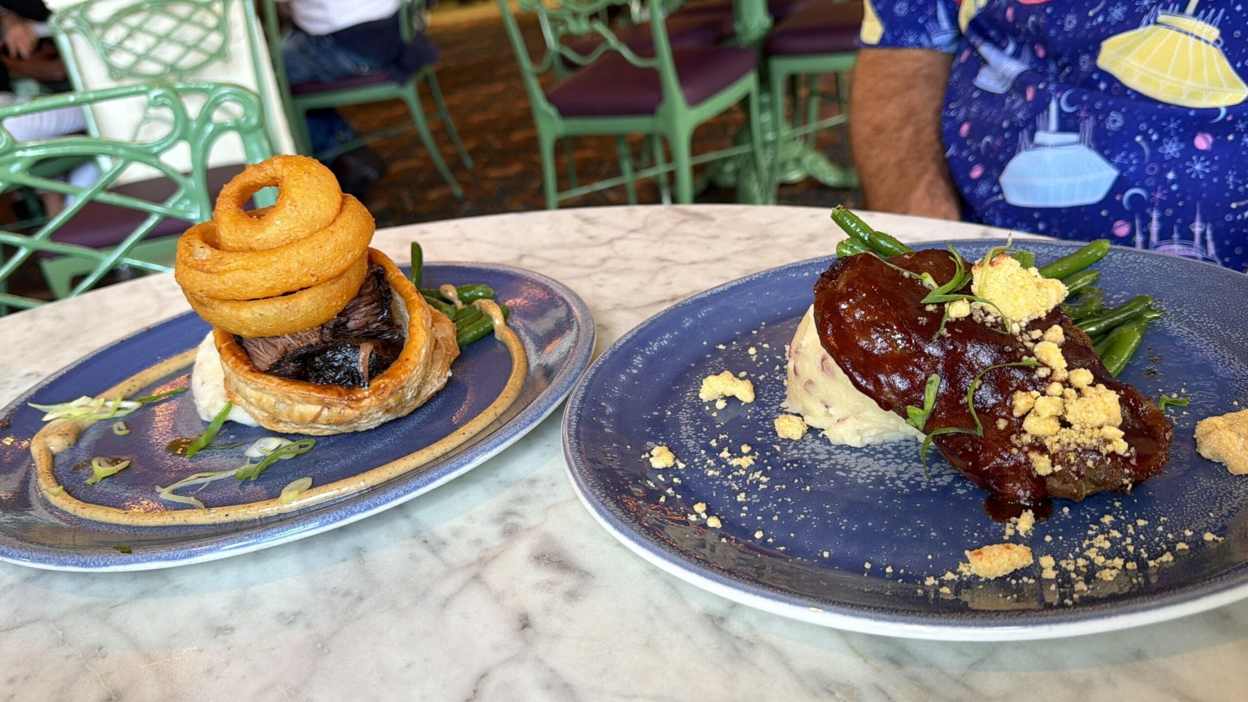 Two blue plates at Disneyland’s Plaza Inn, each with entrees topped with onion rings and green beans, ready for a food review!