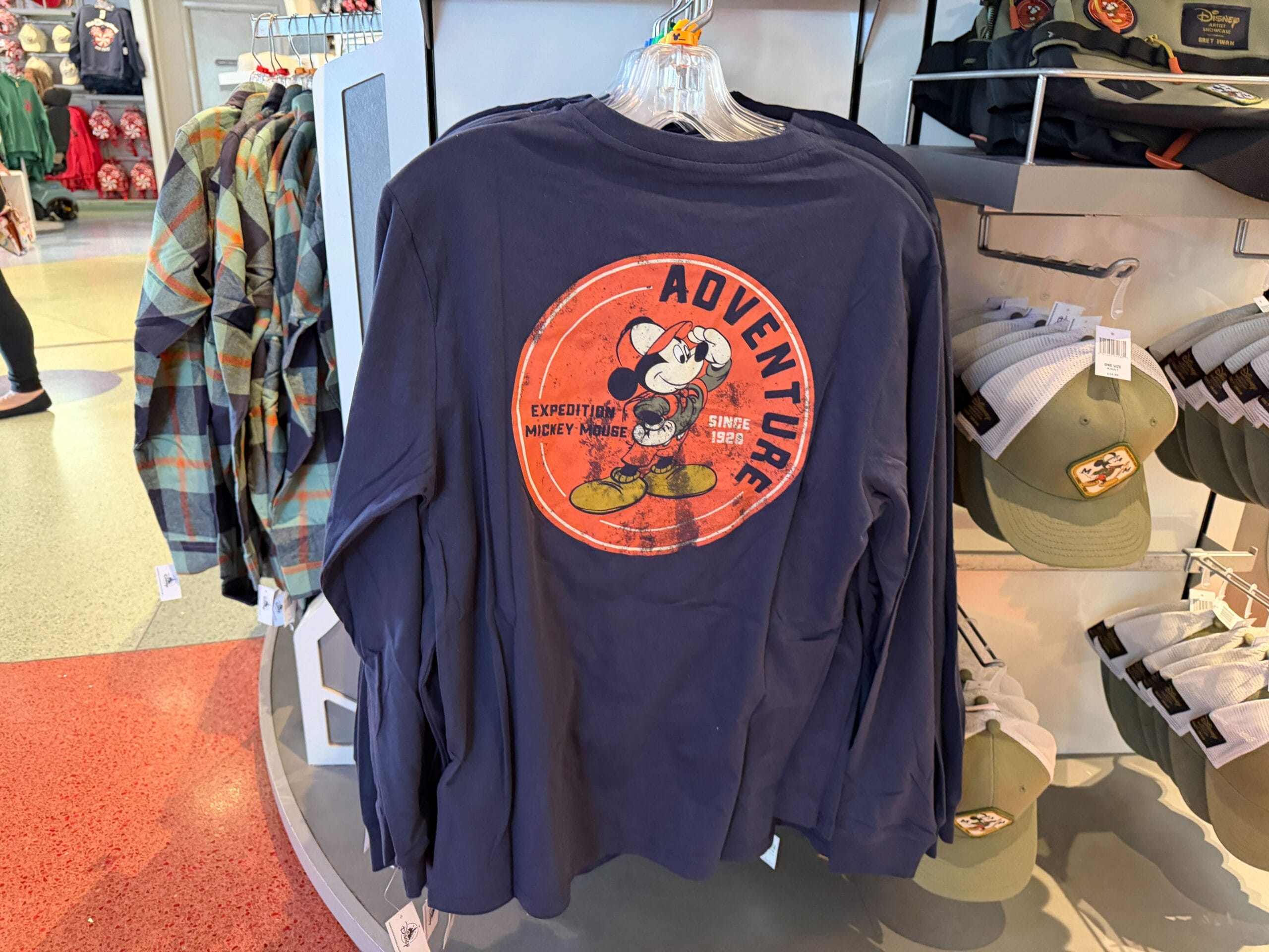Navy long-sleeve shirt from the Mickey Mouse Collection with "Adventure Expedition" graphic, seen in a Disney park store.
