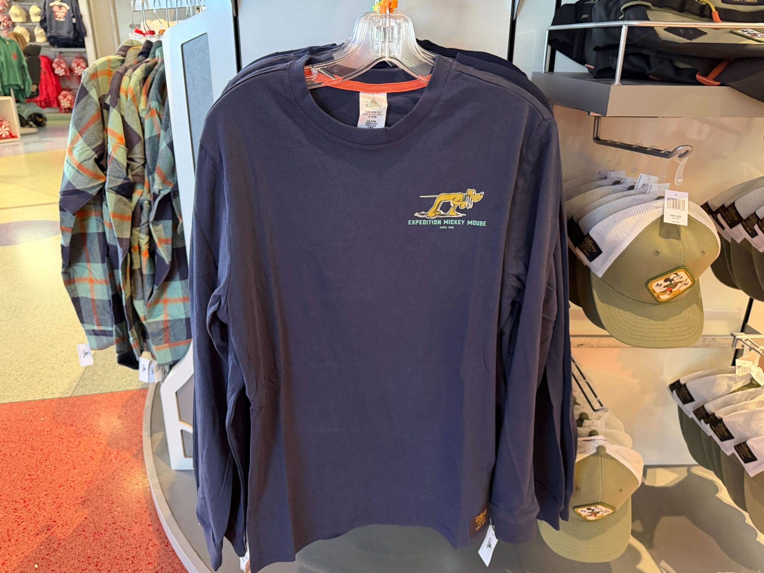 Navy Mickey Mouse Collection long-sleeve shirt with Expedition Everest logo, displayed with hats and plaid shirts in a Disney park shop.