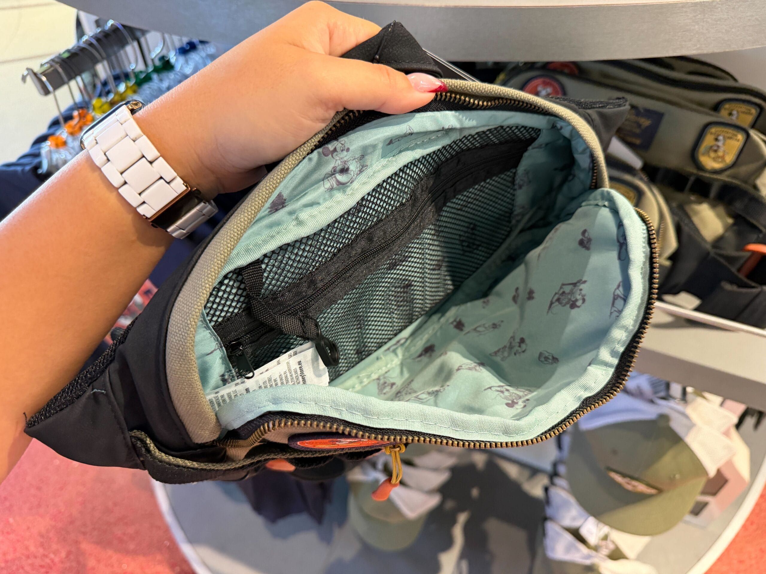 A hand opens a Mickey Mouse Collection bag with dog prints and mesh pockets, perfect for a day at Disney parks worldwide.