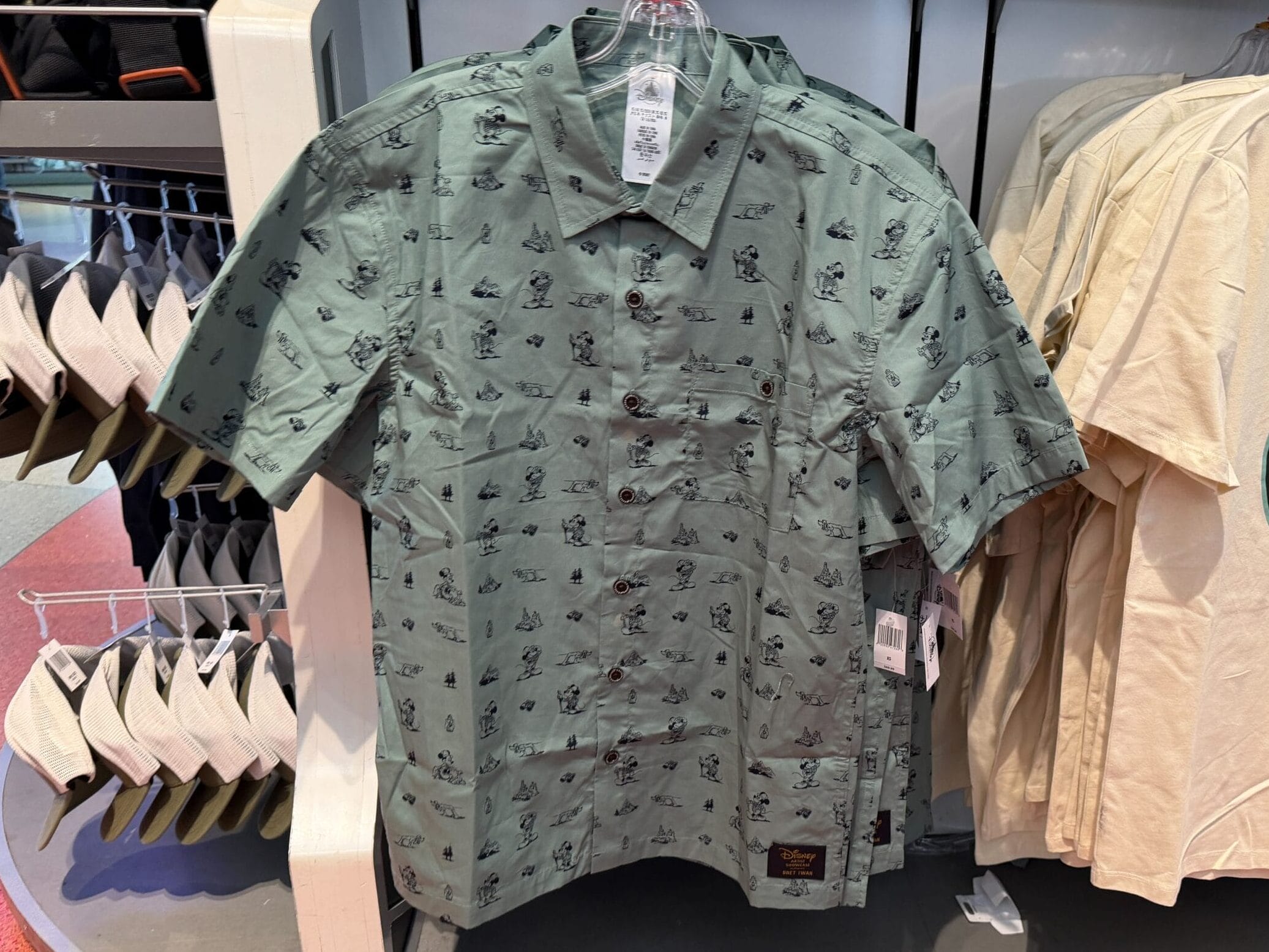 Green button-up with Mickey prints and beige tee from Expedition Mickey Mouse Collection, displayed in a Disney park store.