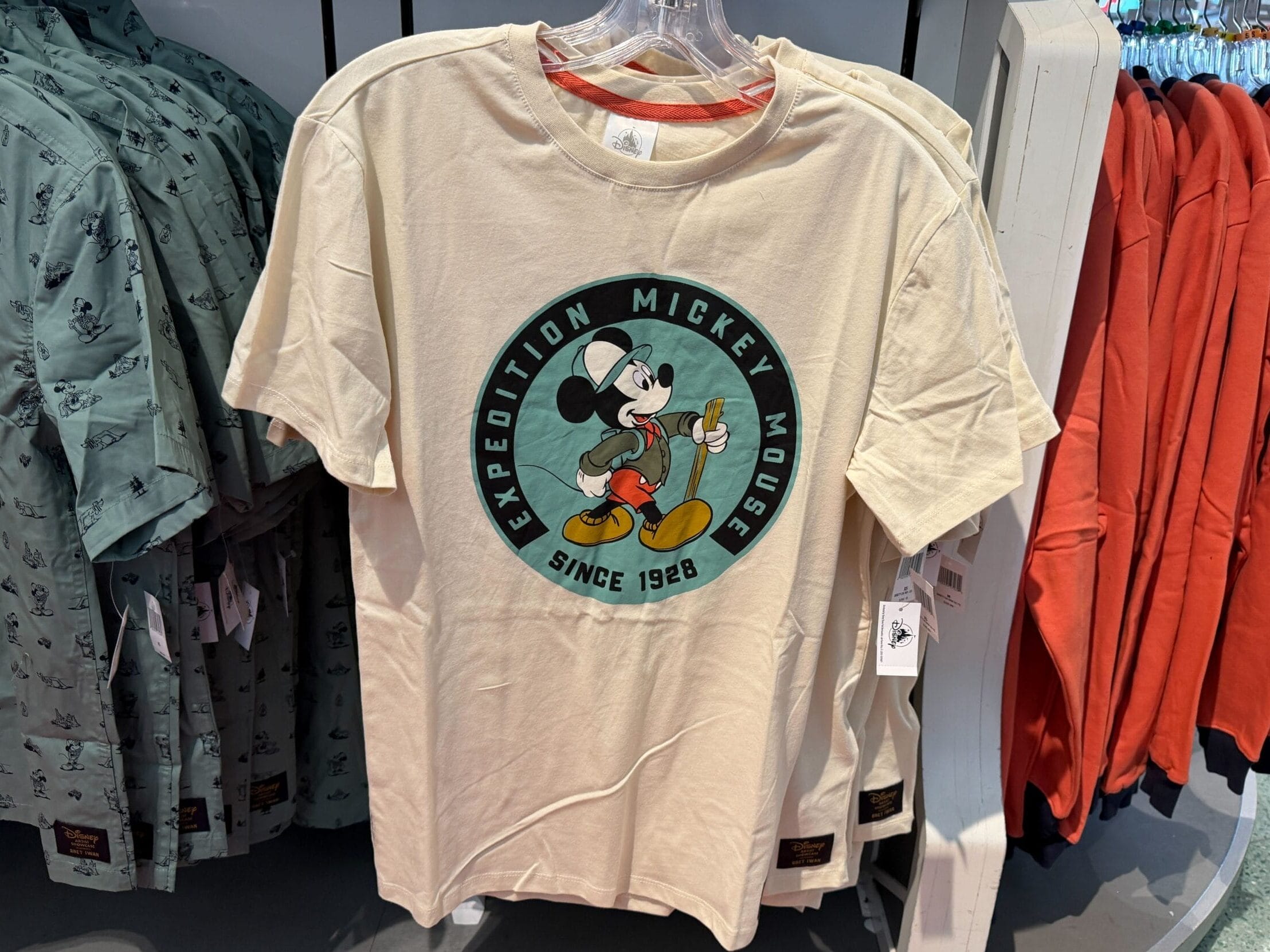 Beige Expedition Collection T-shirt with Mickey Mouse and "Expedition Mickey Mouse Since 1928," seen at a Disney Park store display.