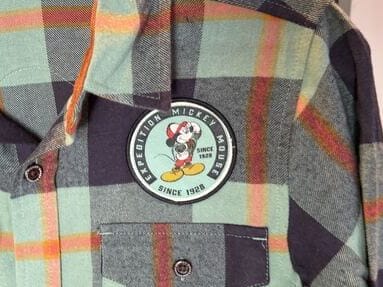 Green, black, and orange plaid shirt from the Mickey Mouse Collection with a Bret Iwan Mickey patch—classic Disney park style.