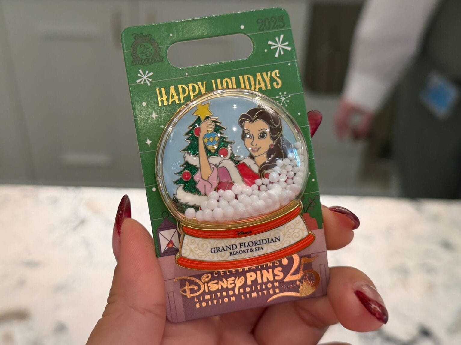 A hand displays a Walt Disney World holiday pin with Belle in a snow globe at Grand Floridian, no castle like Cinderella’s in sight.