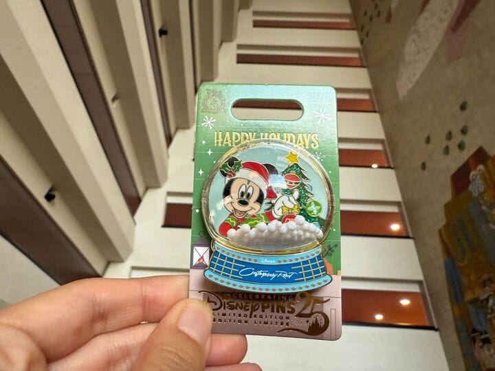 A hand displays a Walt Disney World Holiday Pin of Mickey, Donald, and Goofy in festive outfits with "Happy Holidays" text.