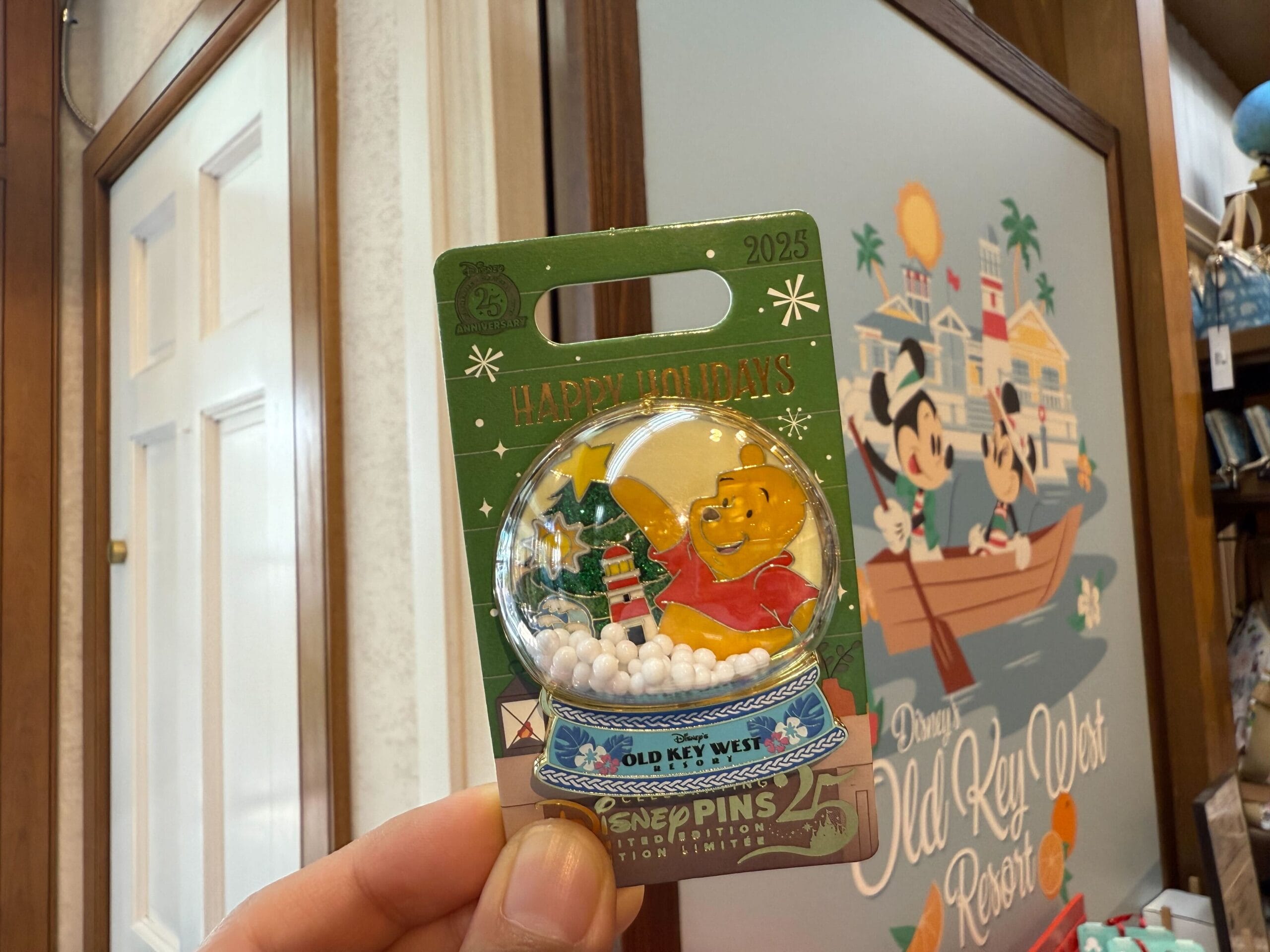 Hand holding a Walt Disney World holiday pin with Winnie the Pooh in a snow globe, displayed at Old Key West Resort—no castle shown.