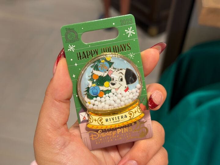 A hand displays a Walt Disney World holiday pin with a Dalmatian puppy, Christmas tree, and decorations—no castle in this design.