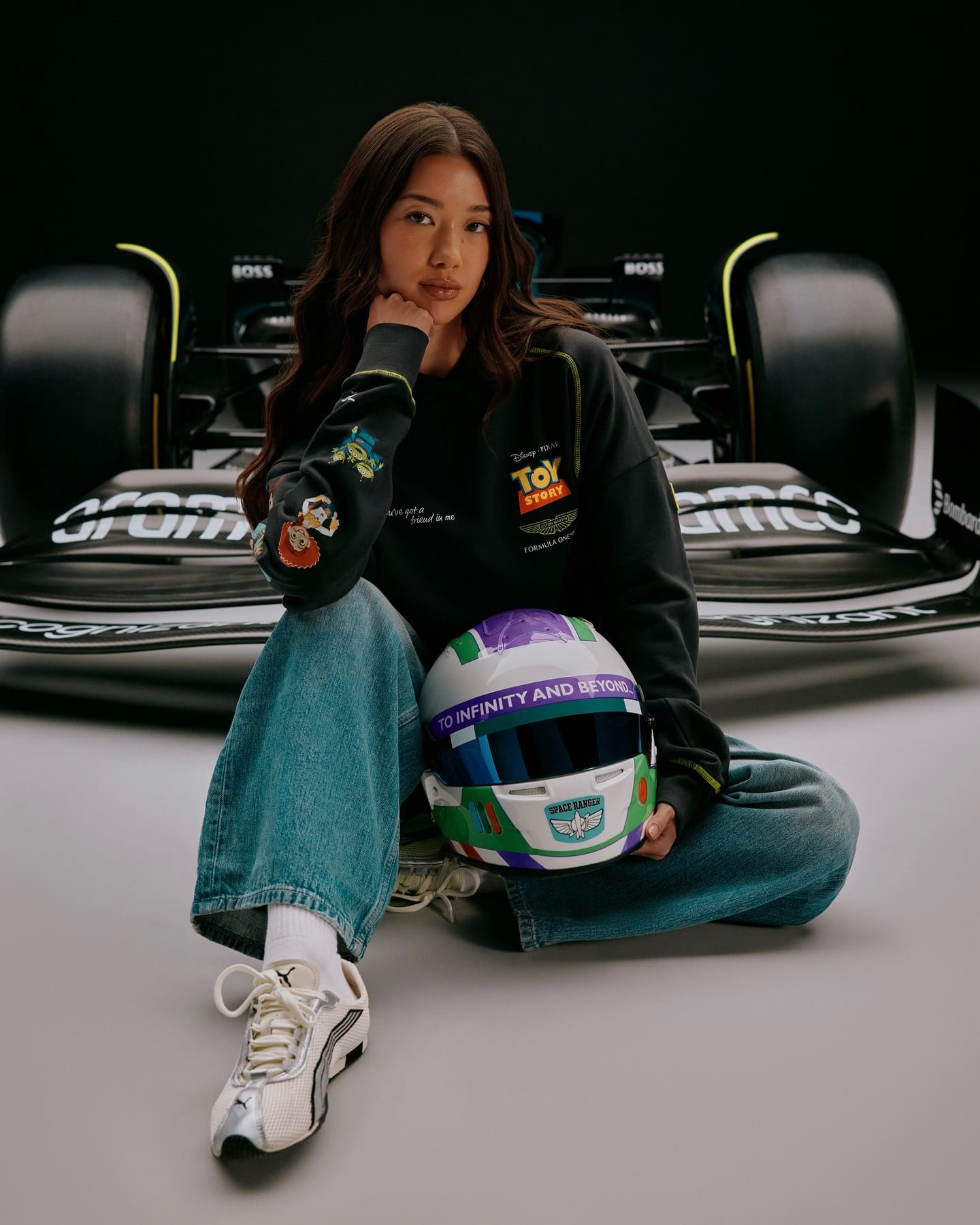 A woman wearing jeans and a Toy Story sweatshirt holds a themed helmet in front of a Formula 1 car, likely at Disney park.