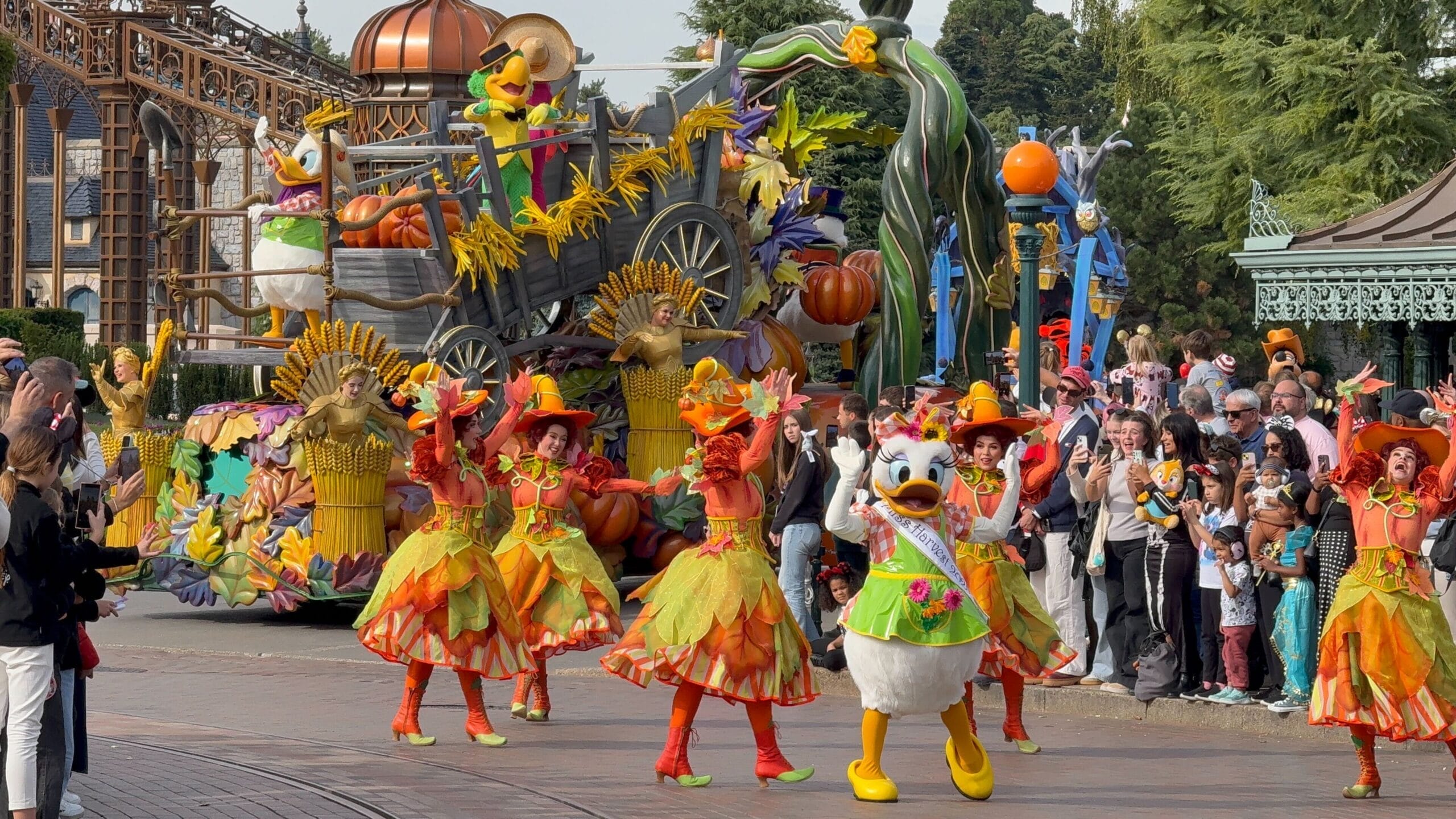 Vibrant Halloween parade at Disneyland Paris 2026, with autumn dancers and a duck mascot leading floats near the fairy-tale castle.