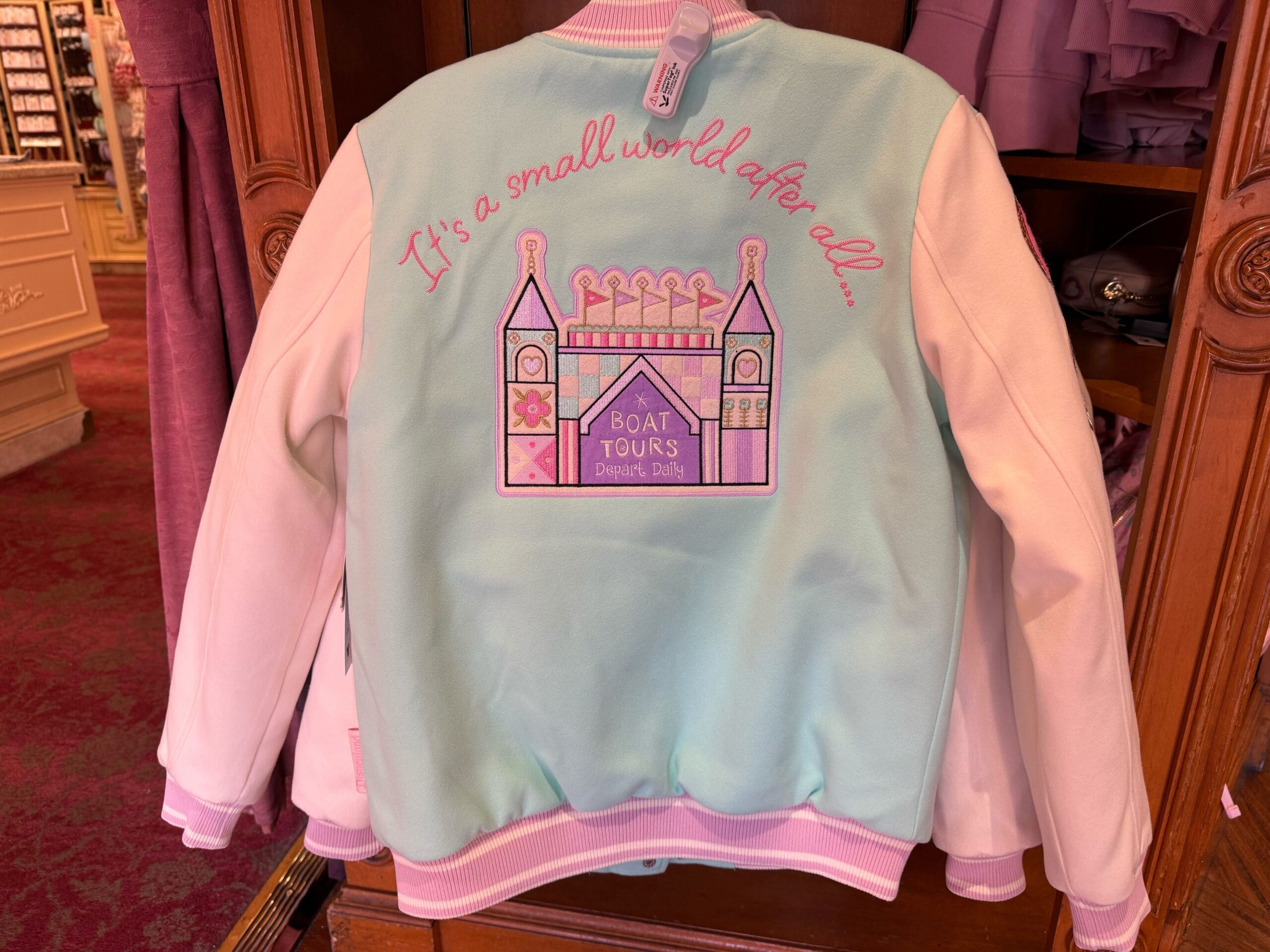 A patch with the ride and "boat tours depart daily" text is on the back. Stitched in pink embroidery above is the text "It's a small world after all..."