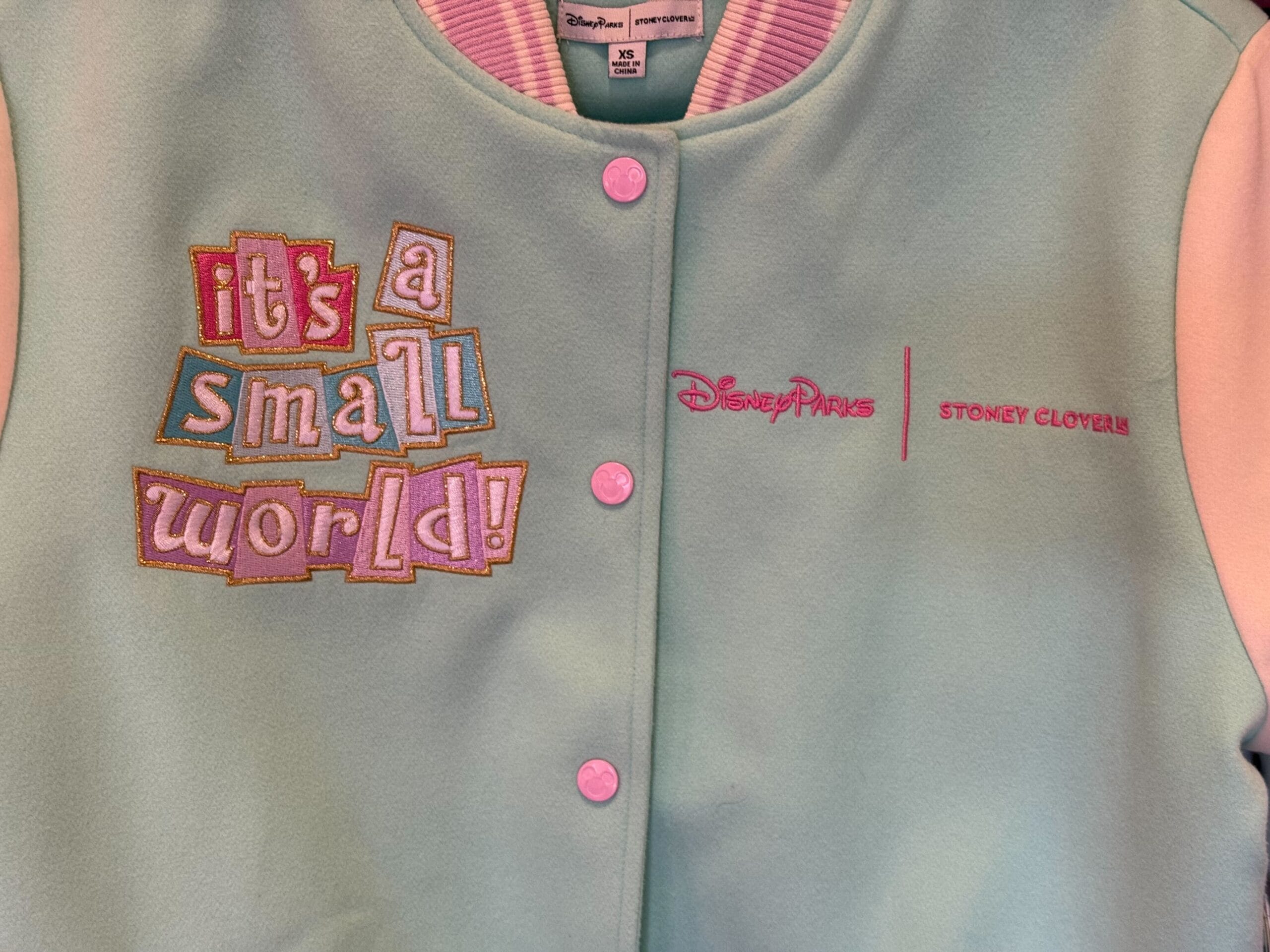 The Letterman-style jacket is pastel blue with pastel pink and purple sleeves, a collar, and a ribbed waistband.