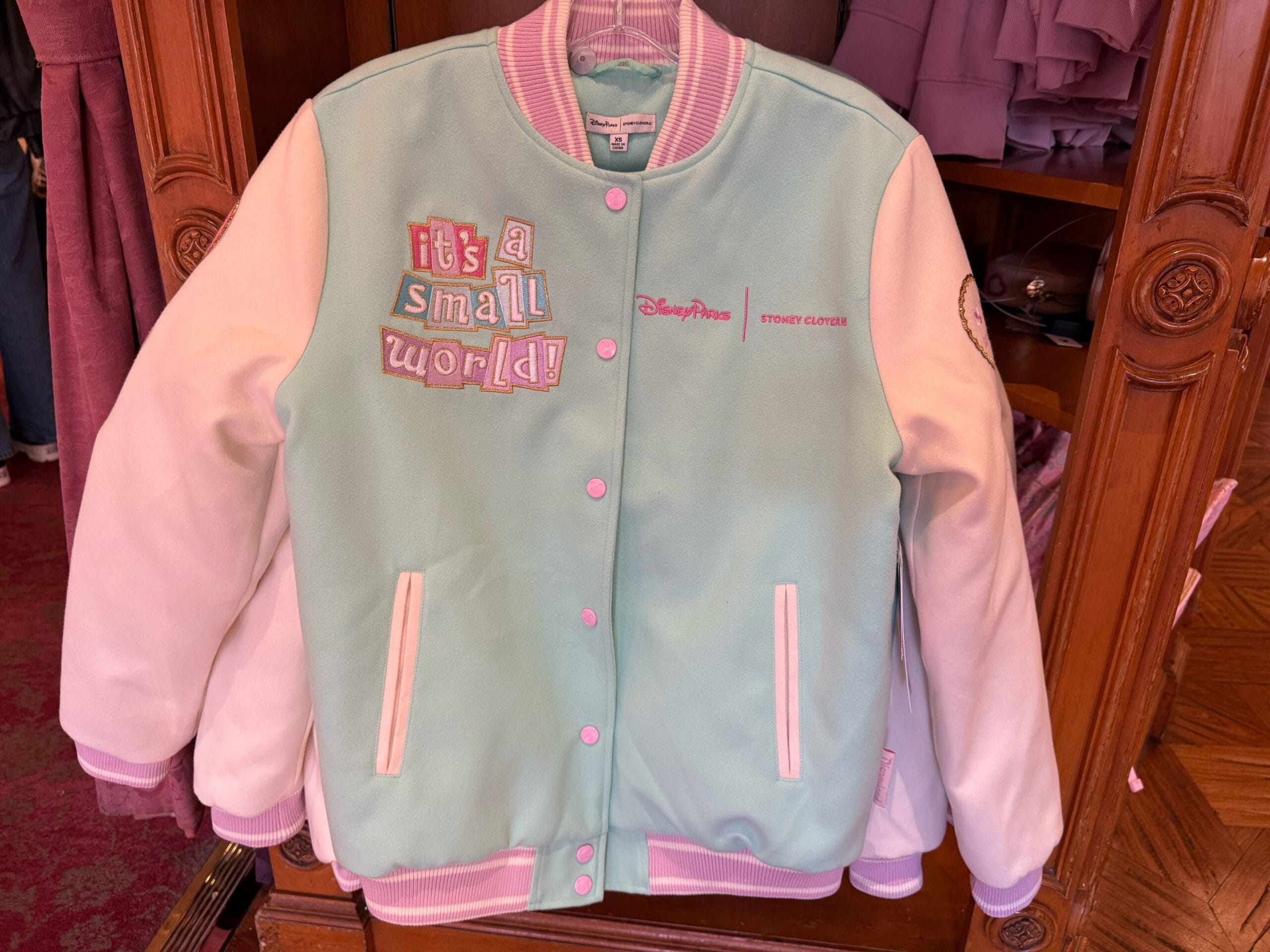 The Letterman-style jacket is pastel blue with pastel pink and purple sleeves, a collar, and a ribbed waistband.