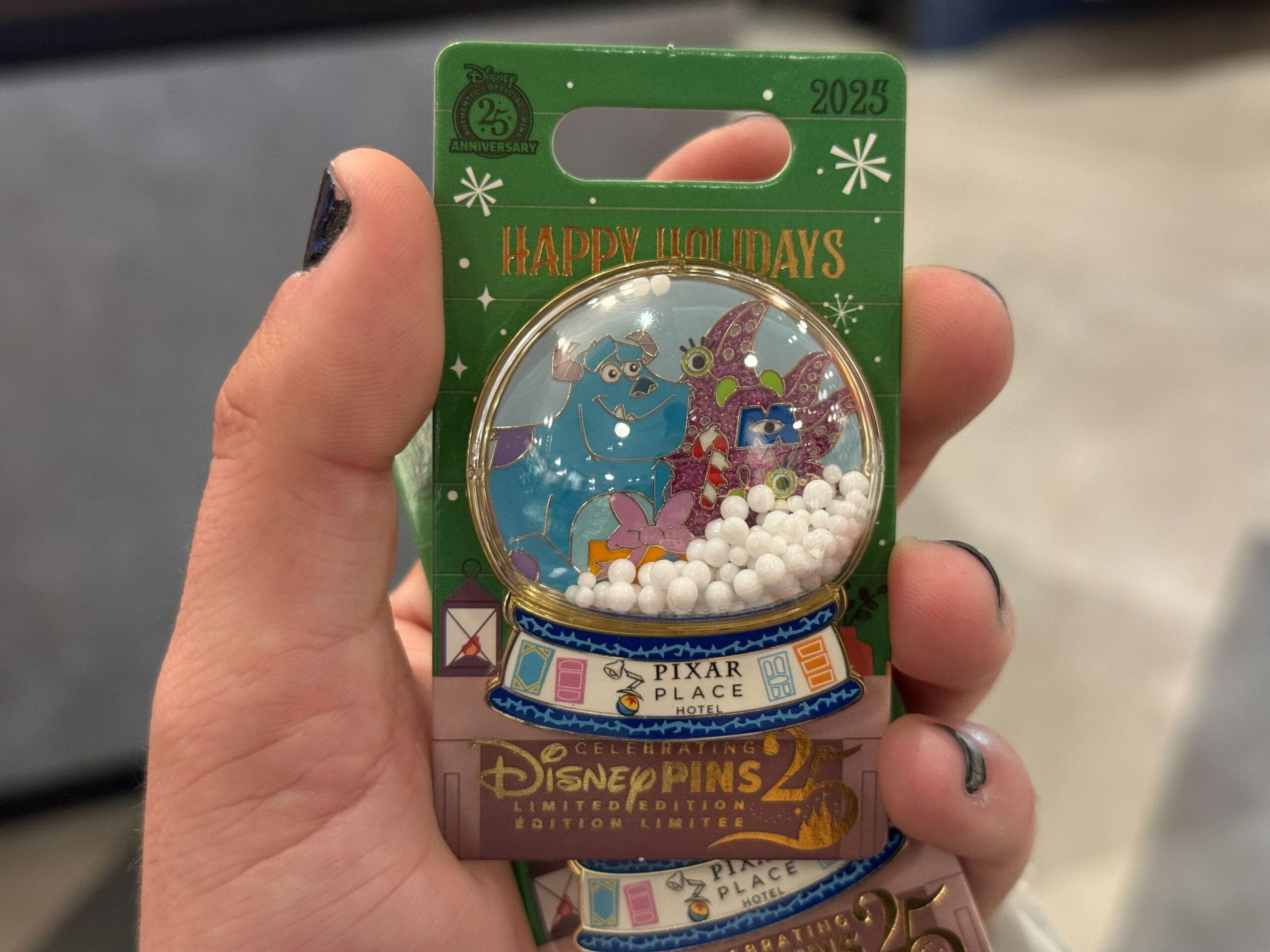 Hand holds a 2025 Monsters, Inc. snow globe holiday pin at Disneyland Resort Hotel