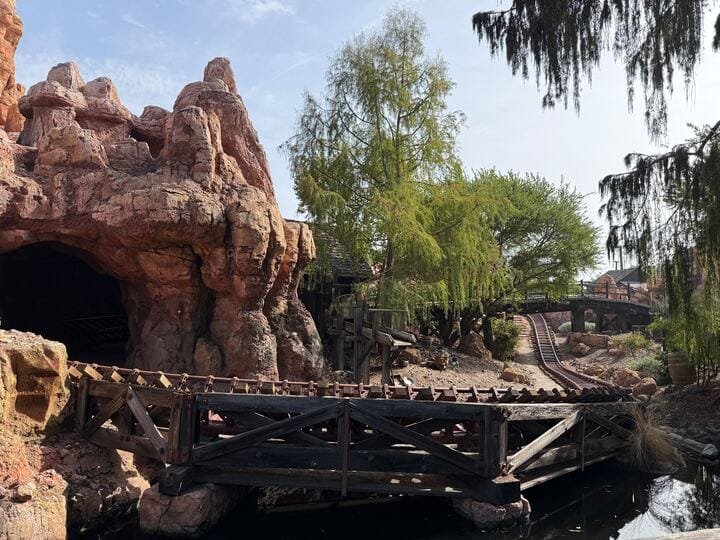 Big Thunder Mountain Railroad’s wooden track twists amid red cliffs and trees at Disneyland, with no castle in this view.